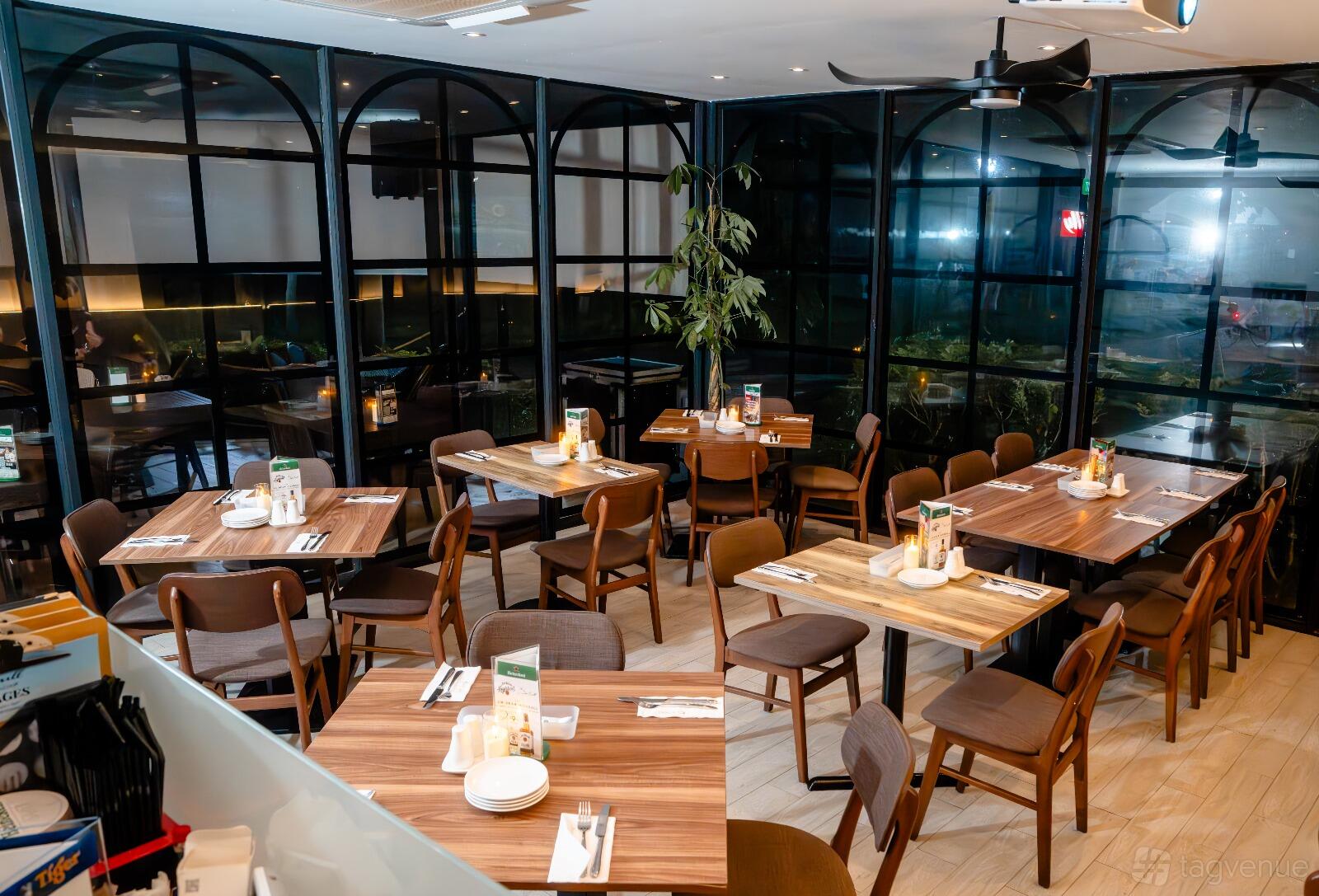 A restaurant dining area with wooden tables, brown chairs, and floor-to-ceiling windows at The Seagrill.