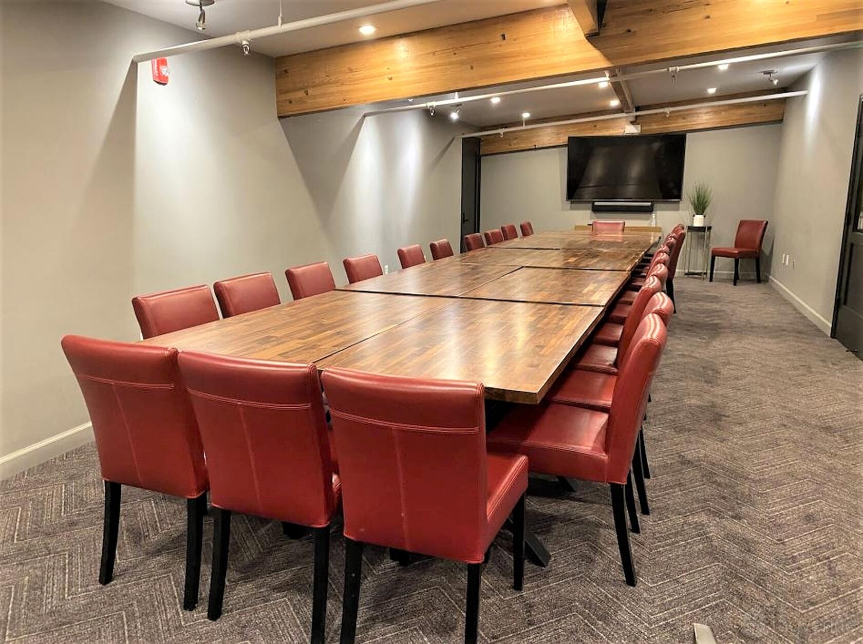 An event venue with a long wooden conference table, red upholstered chairs, and a large wall-mounted TV at Domenico Winery.