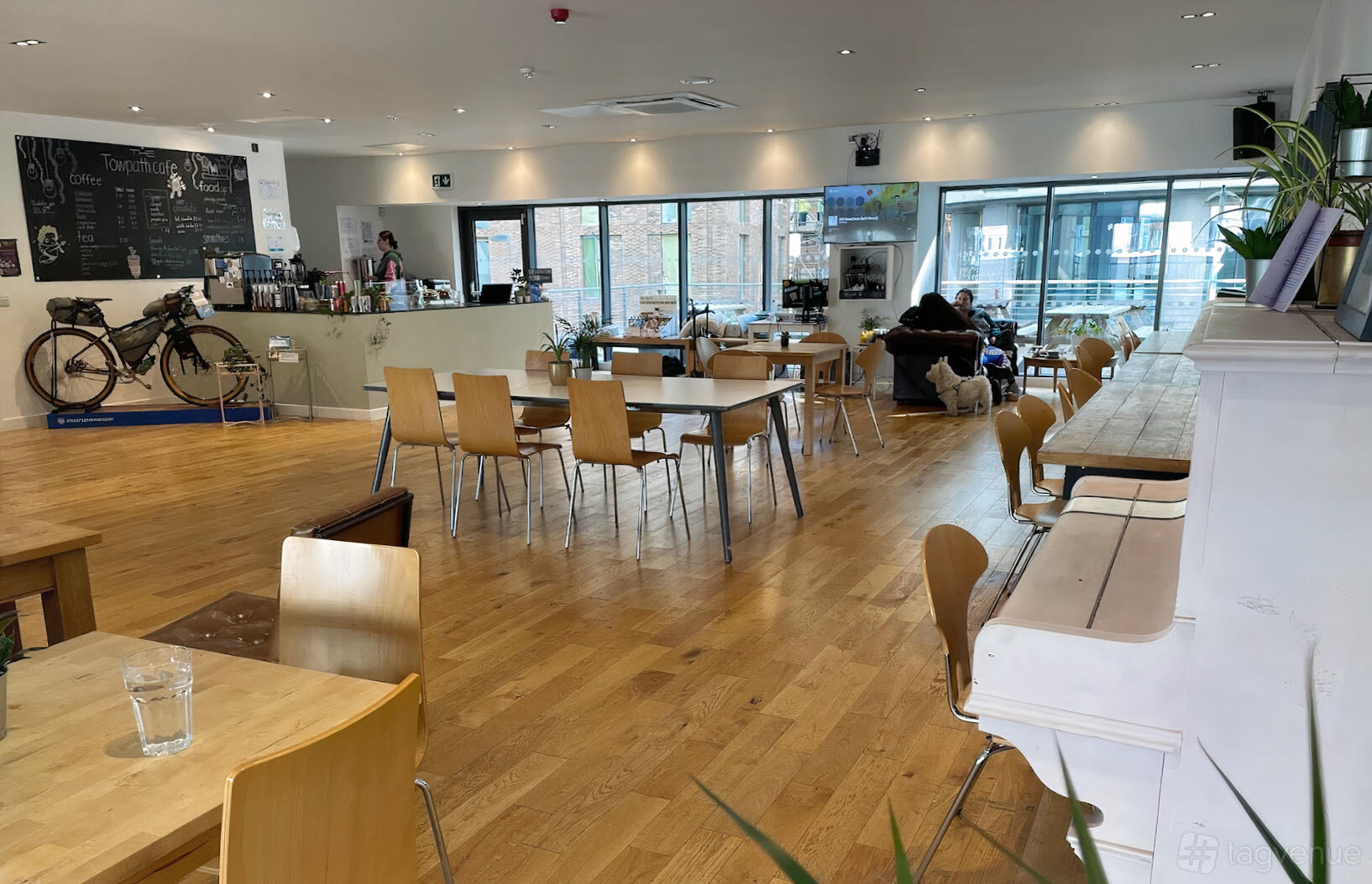 An event space in a cafe with wooden floors, light wood tables and chairs, chalkboard menu, and large windows at The Towpath Cafe.