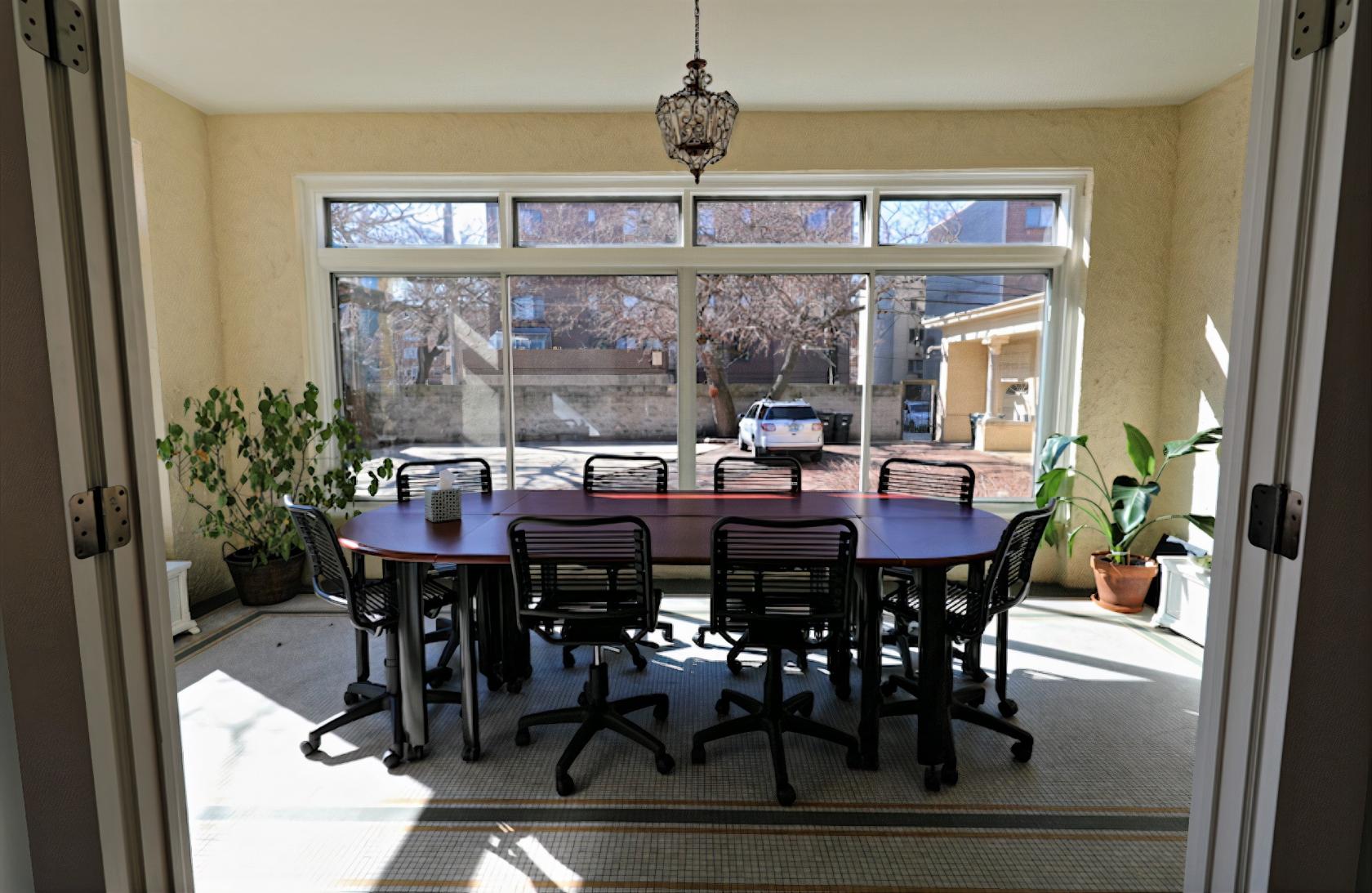 A conference room with floor-to-ceiling windows, potted plants, and a long table with office chairs at Colvin House.