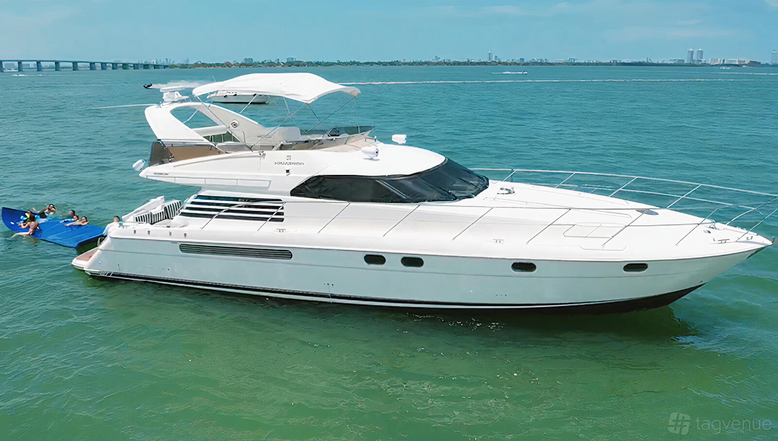A sleek white yacht with an upper flybridge deck and shaded seating area on the water at Jerico Yacht Charters.