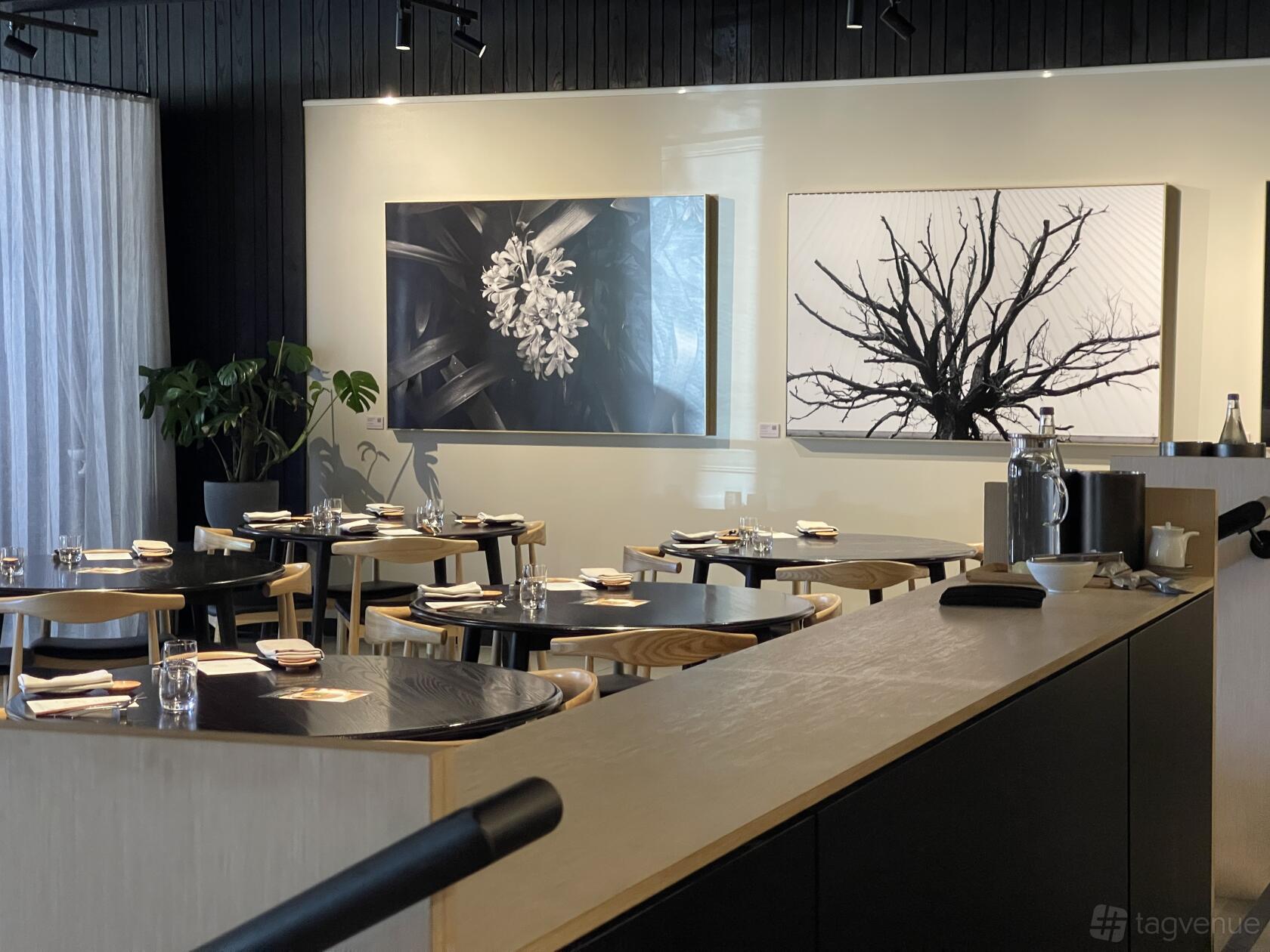 A restaurant with wooden tables, minimalist black chairs, and contemporary monochrome artwork at KOMEYUI Melbourne.