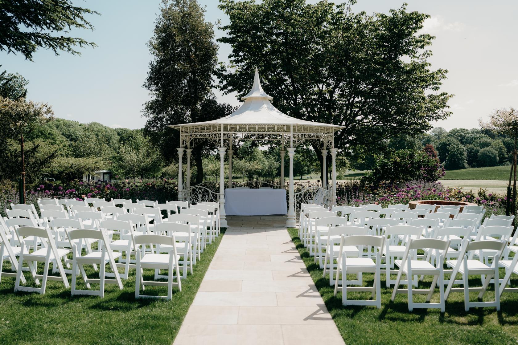 A country house garden hall with a white gazebo, rows of white chairs, and lush greenery at Norwood Park Country House.