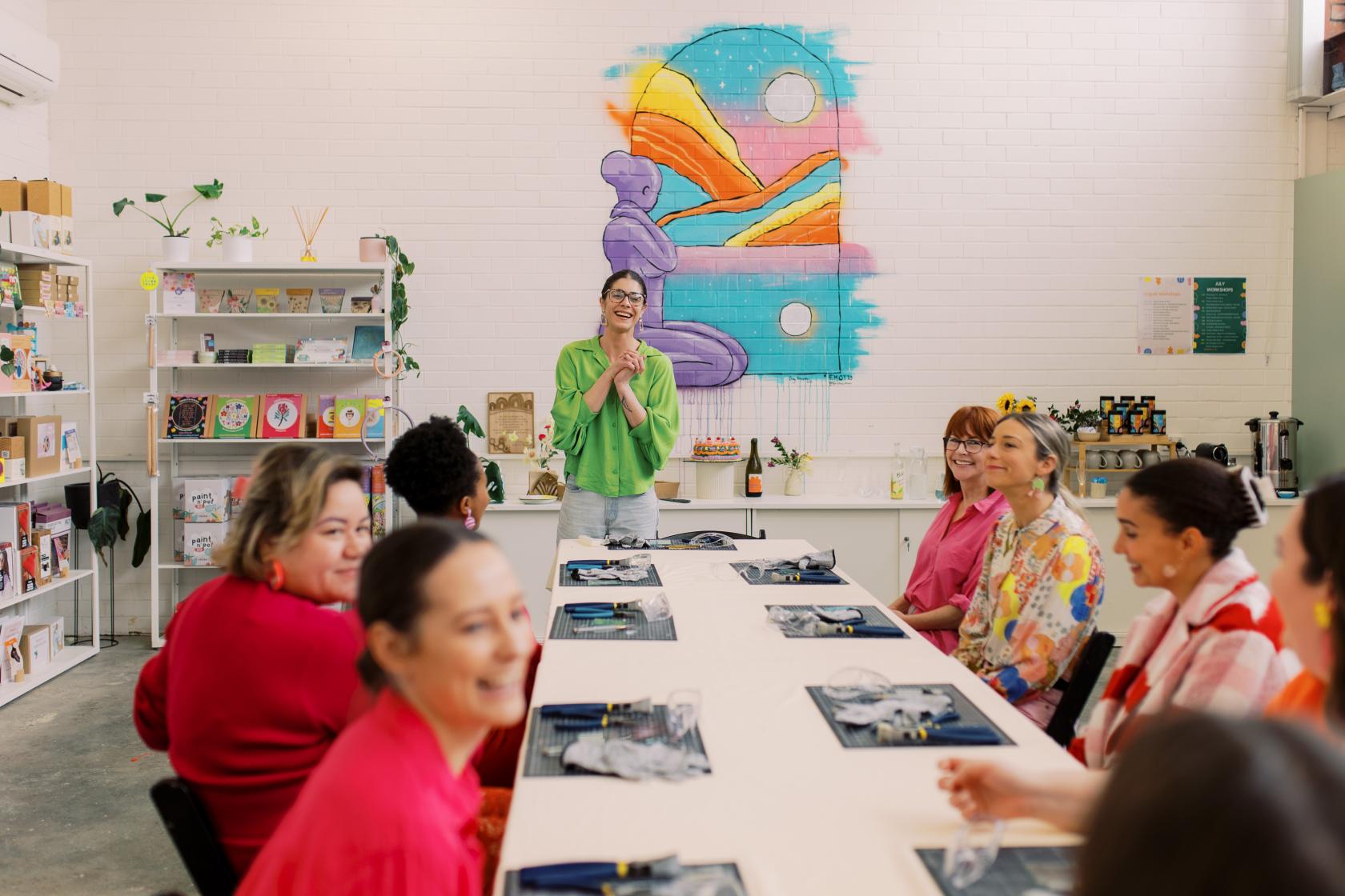 A creative space with a long table set for a workshop, colorful mural, and art supplies at Hobby Studio.