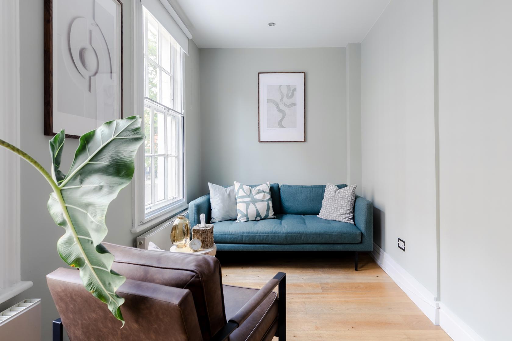 A meeting centre with a teal sofa, armchair, large windows, and abstract wall art at CuraRooms Marylebone.
