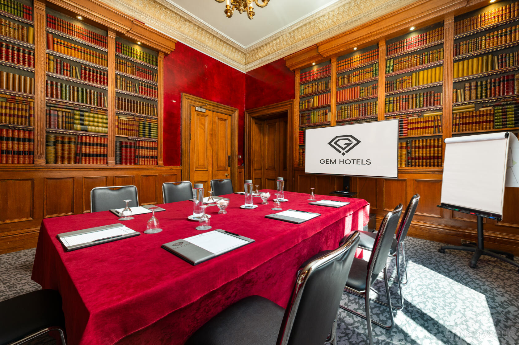 An event space with a red velvet-draped meeting table, leather chairs, and walls lined with bookshelves at Strathmore Hotel.