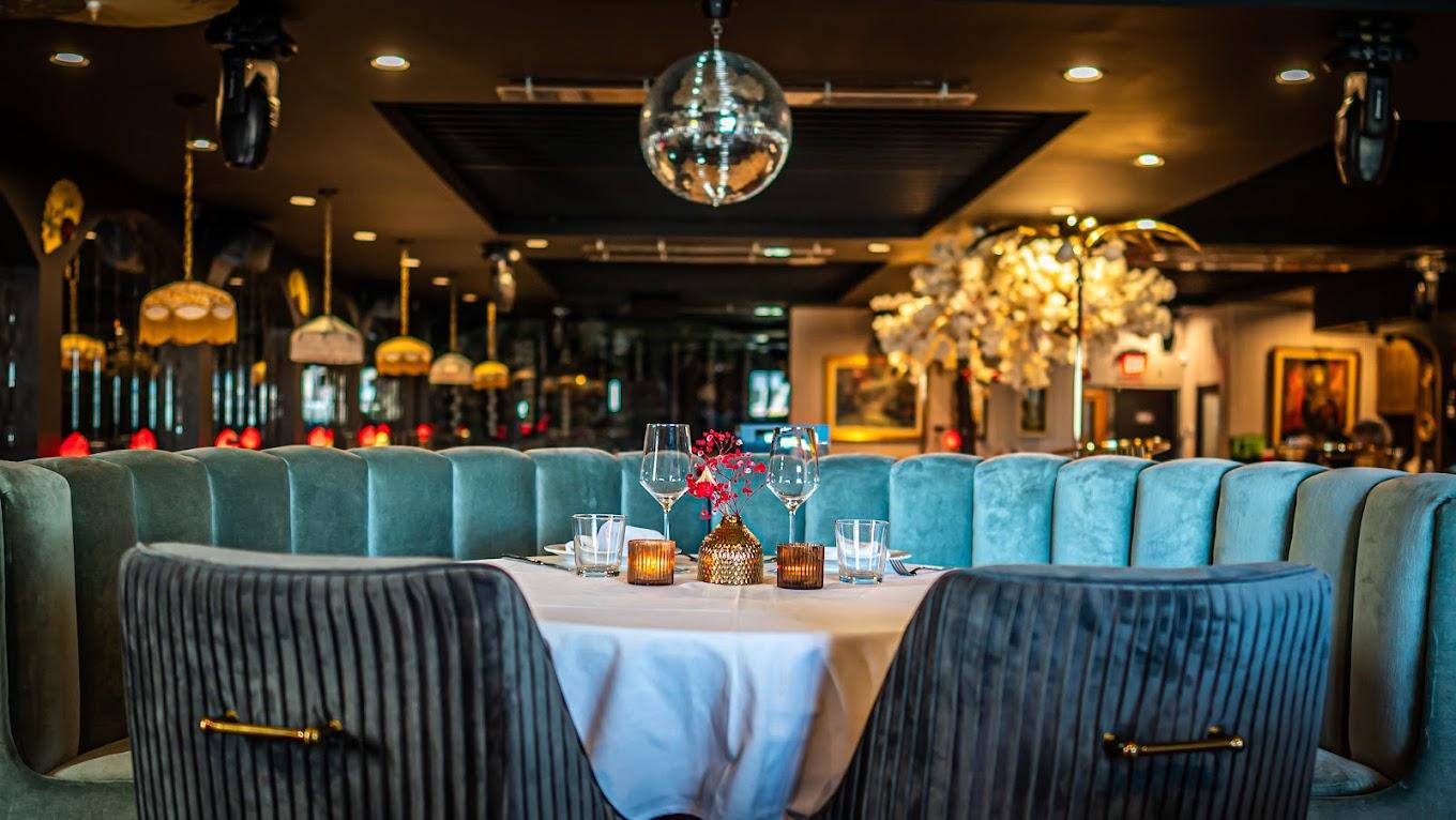 A restaurant with velvet banquette seating, round table settings, and disco ball lighting at ADKT LA.