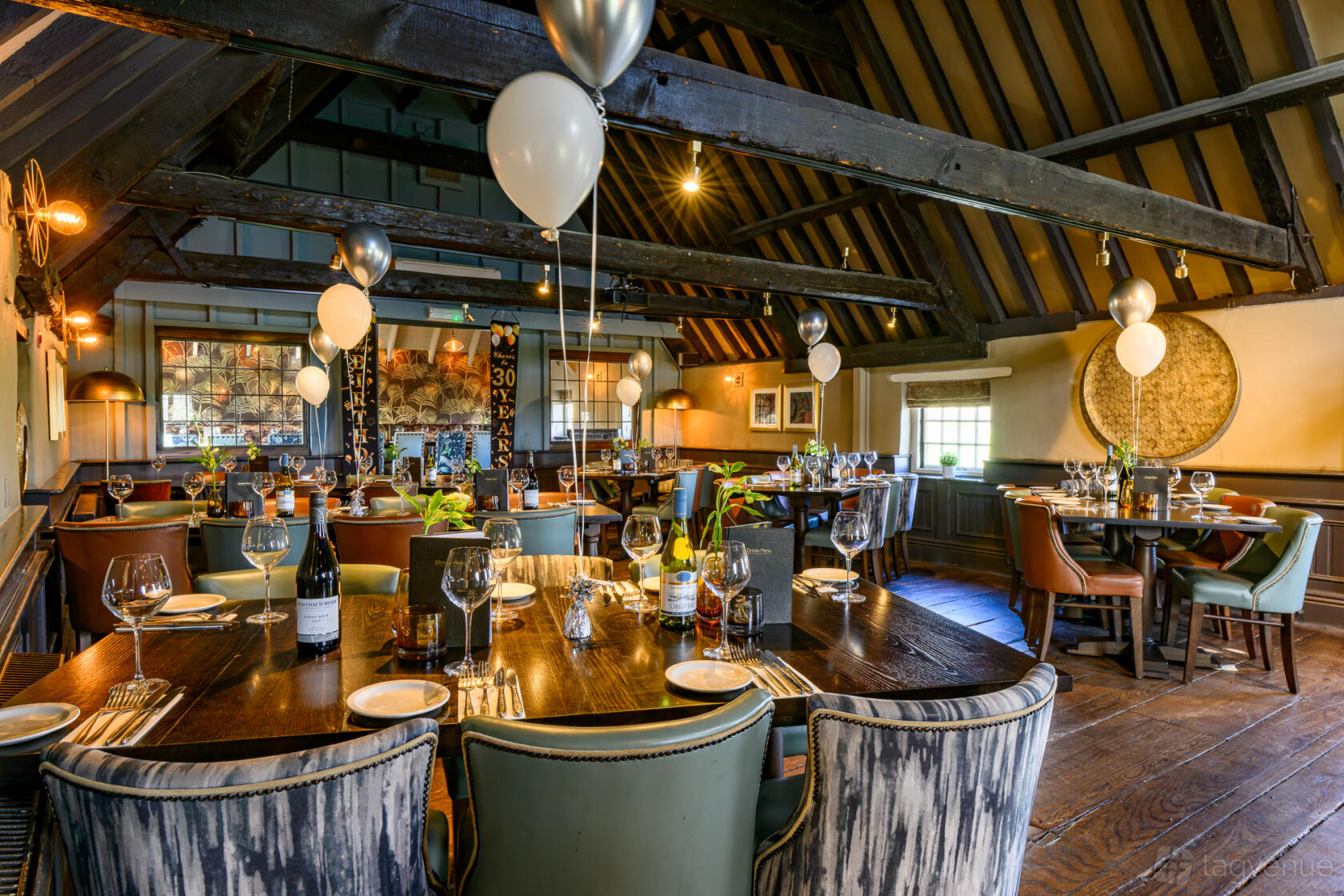 A dining room with exposed wooden beams, decorated tables, and balloons at Brampton Mill.