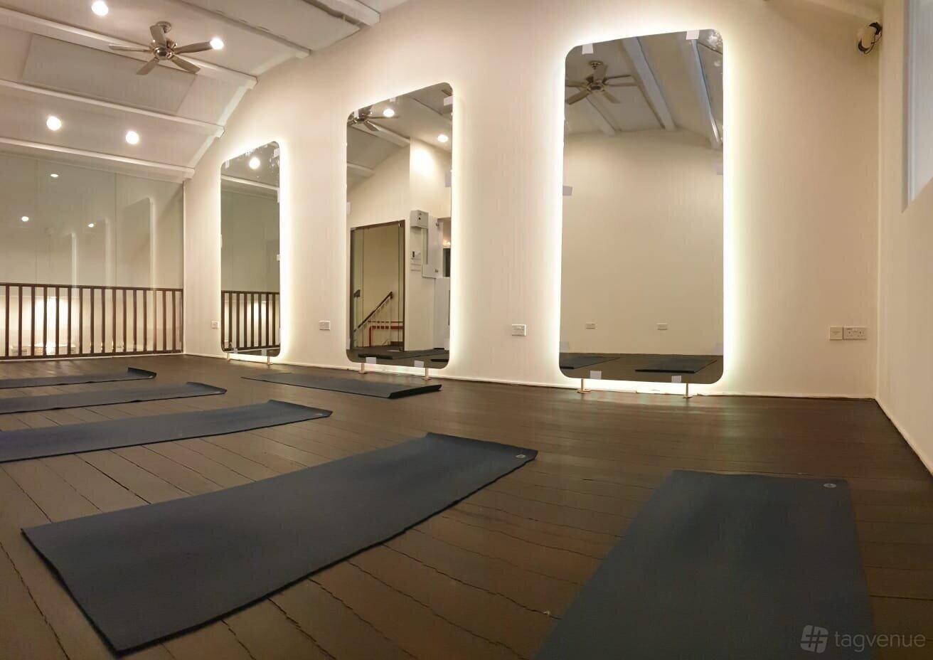 A dance studio with dark wooden floors, yoga mats, tall mirrors, and ceiling fans at Shiva Yoga Studio.