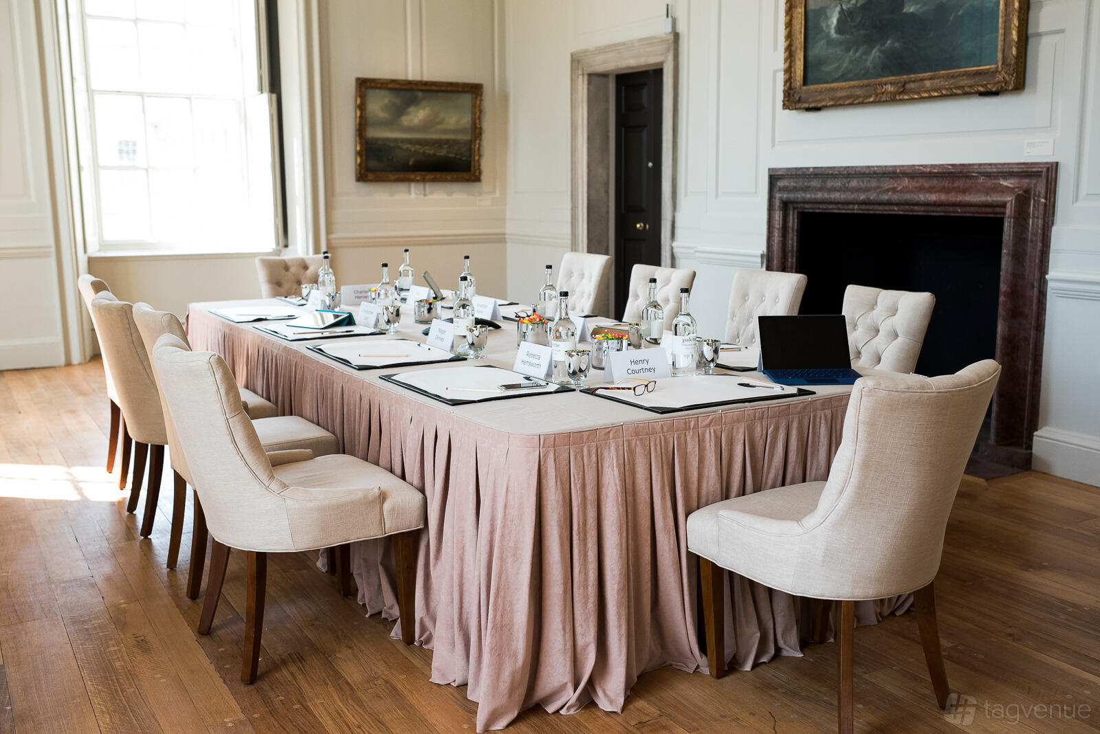 A function room with tufted chairs, a skirted meeting table, wood floors, and large windows at The Queen's House.