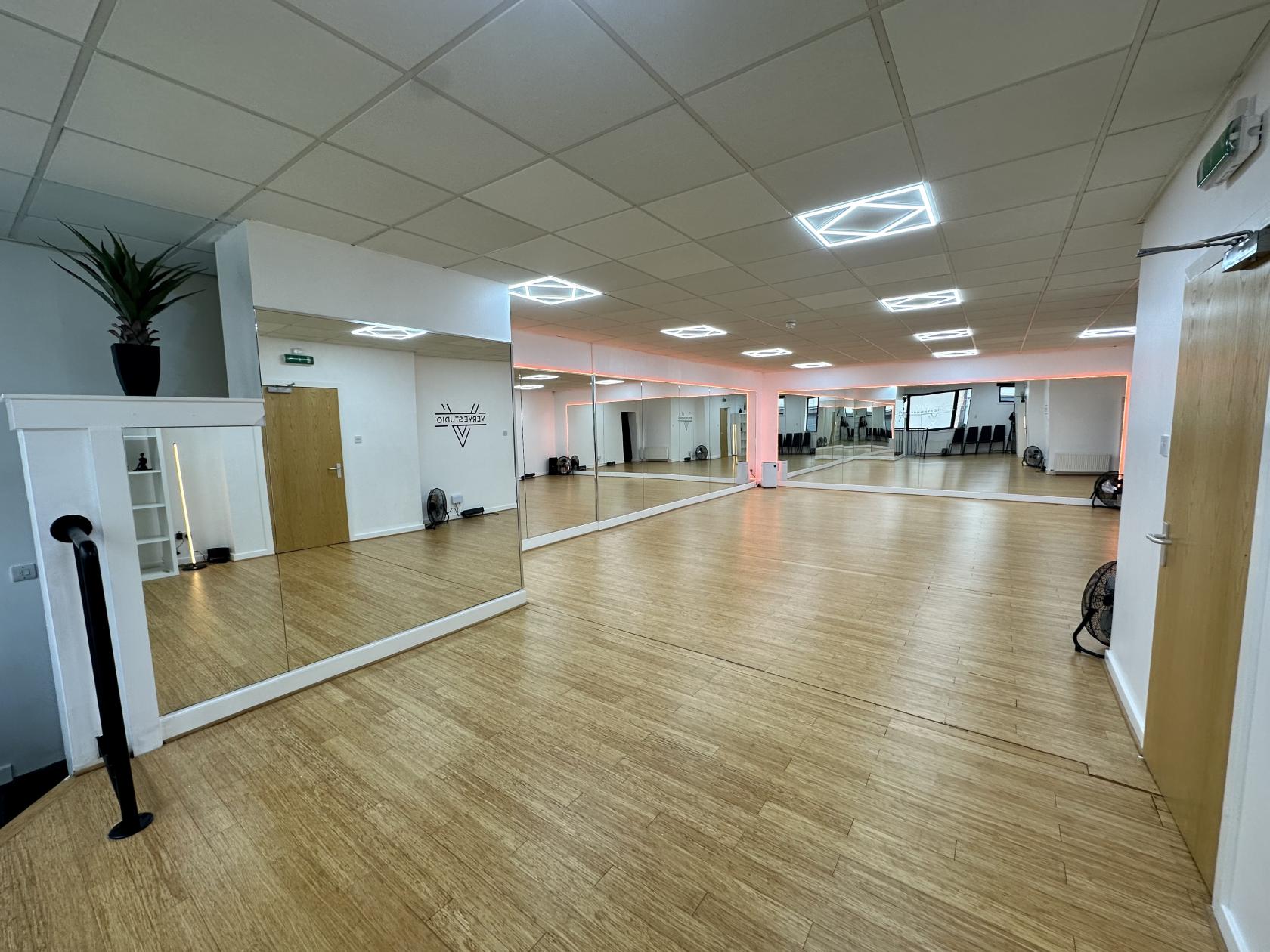 A rehearsal studio with mirrored walls, wood flooring, and geometric ceiling lights at Verve Studio.