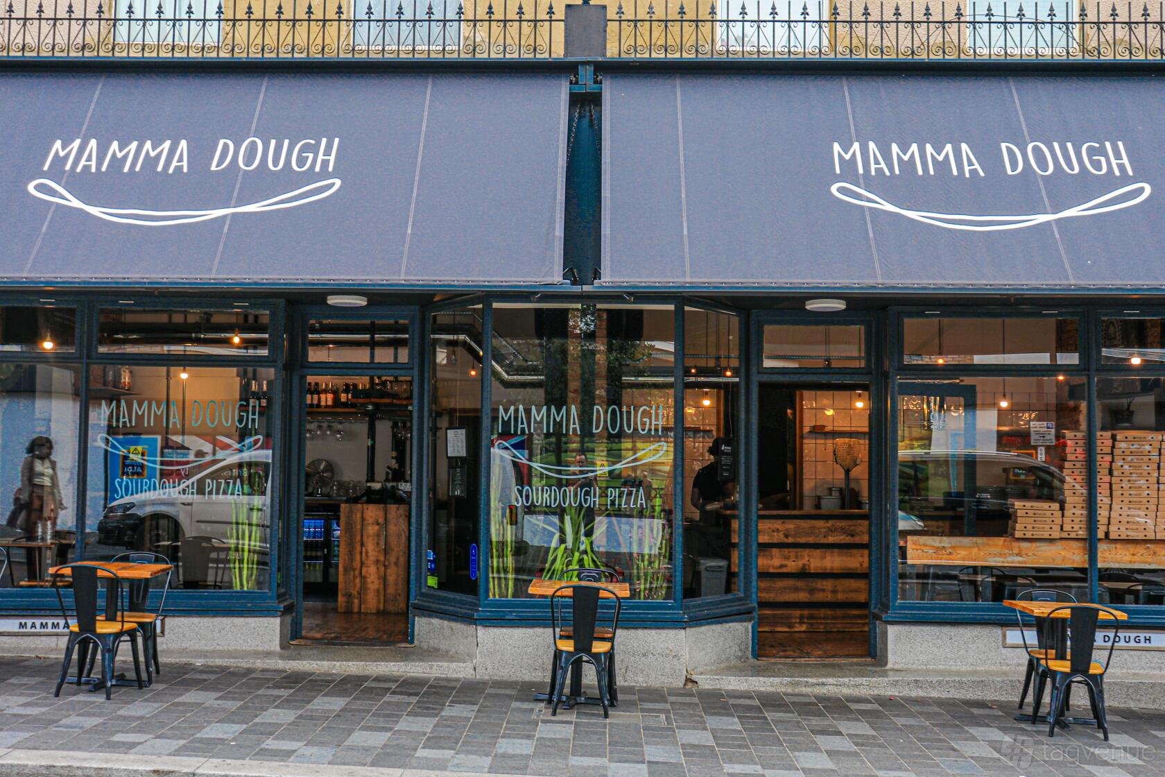 A restaurant exterior with blue-framed windows, open doors, and outdoor seating at Mamma Dough South Norwood.
