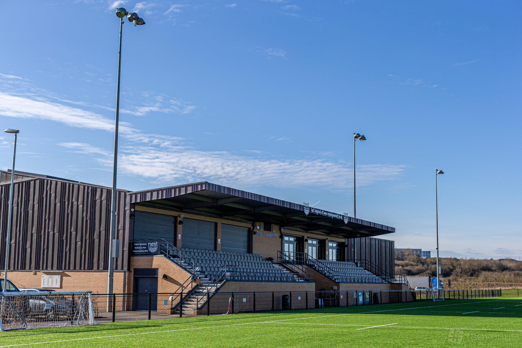 An event space with outdoor bleacher seating, covered spectator stands, and artificial turf at Shaftesbury Park.