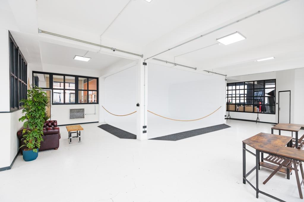 A photo studio with white walls, grid windows, ceiling lights, potted plant, and wooden tables at Spectrum Studios.