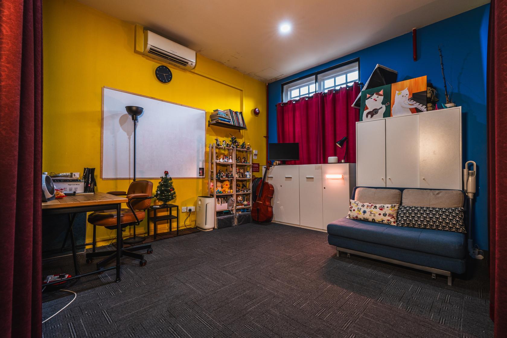 A music studio with yellow and blue walls, red curtains, a whiteboard, and a sofa at Anadigi.