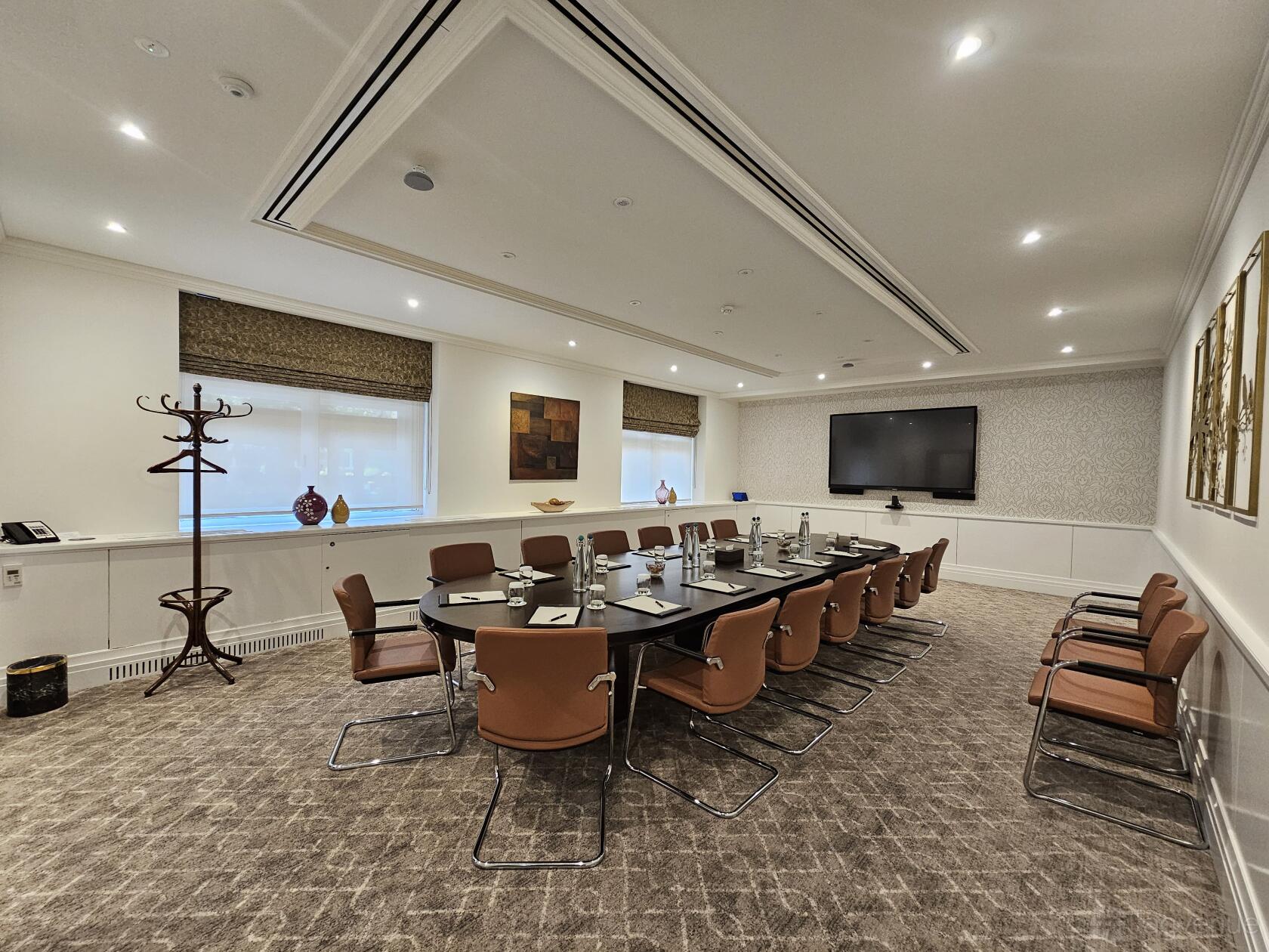 A hotel boardroom with a long conference table, brown leather chairs, wall-mounted display, and large windows at St. James Court, a Taj Hotel.