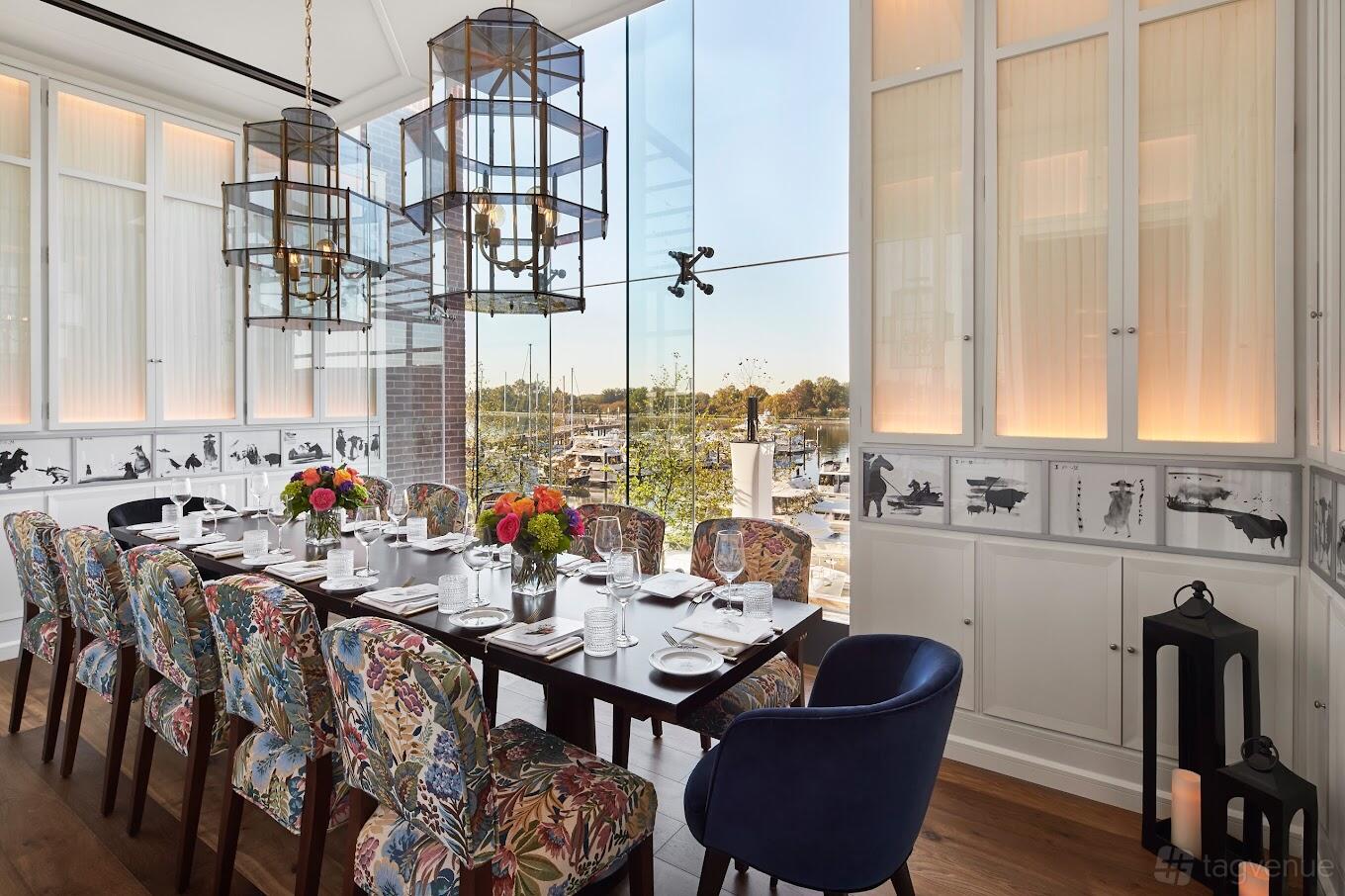 A dining room with floral upholstered chairs, large glass windows, and hanging lanterns at Del Mar.