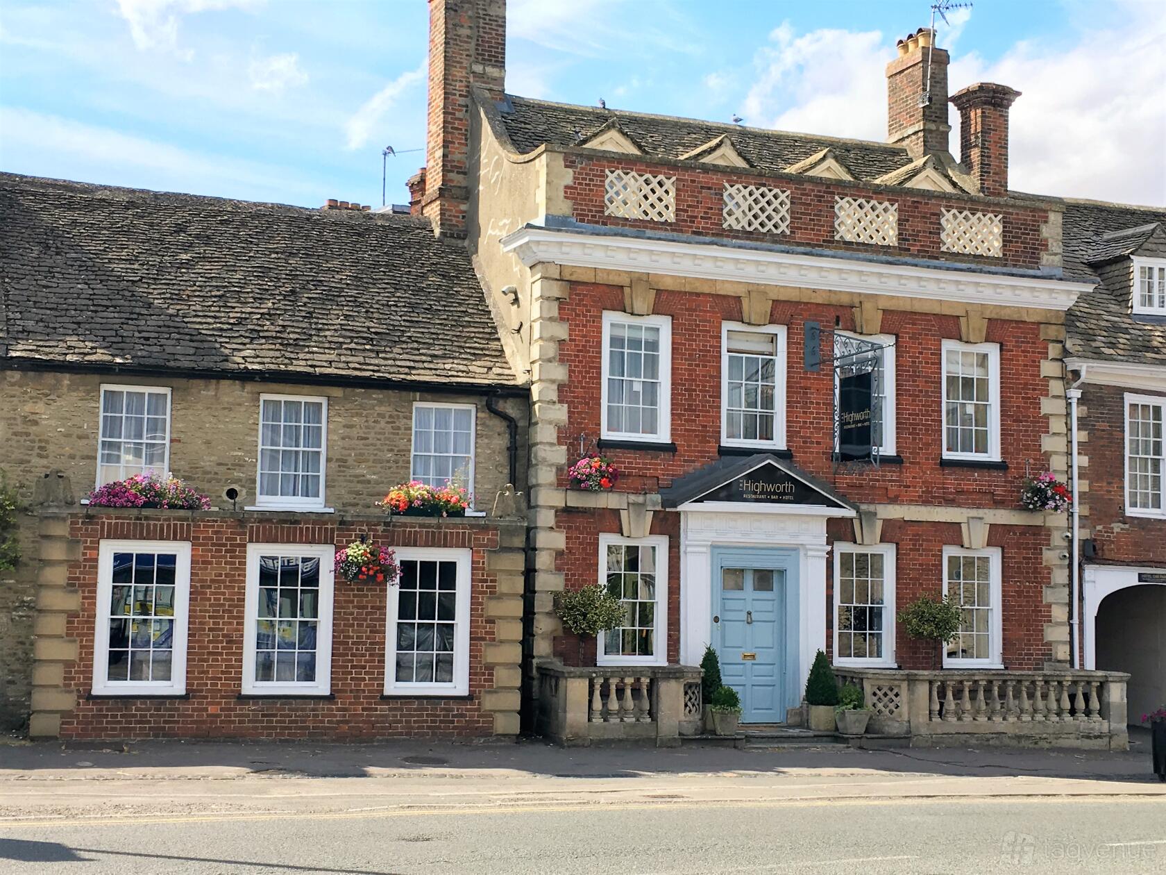 A hotel with a Georgian brick facade, light blue door, sash windows, and hanging flower baskets at The Highworth Hotel.