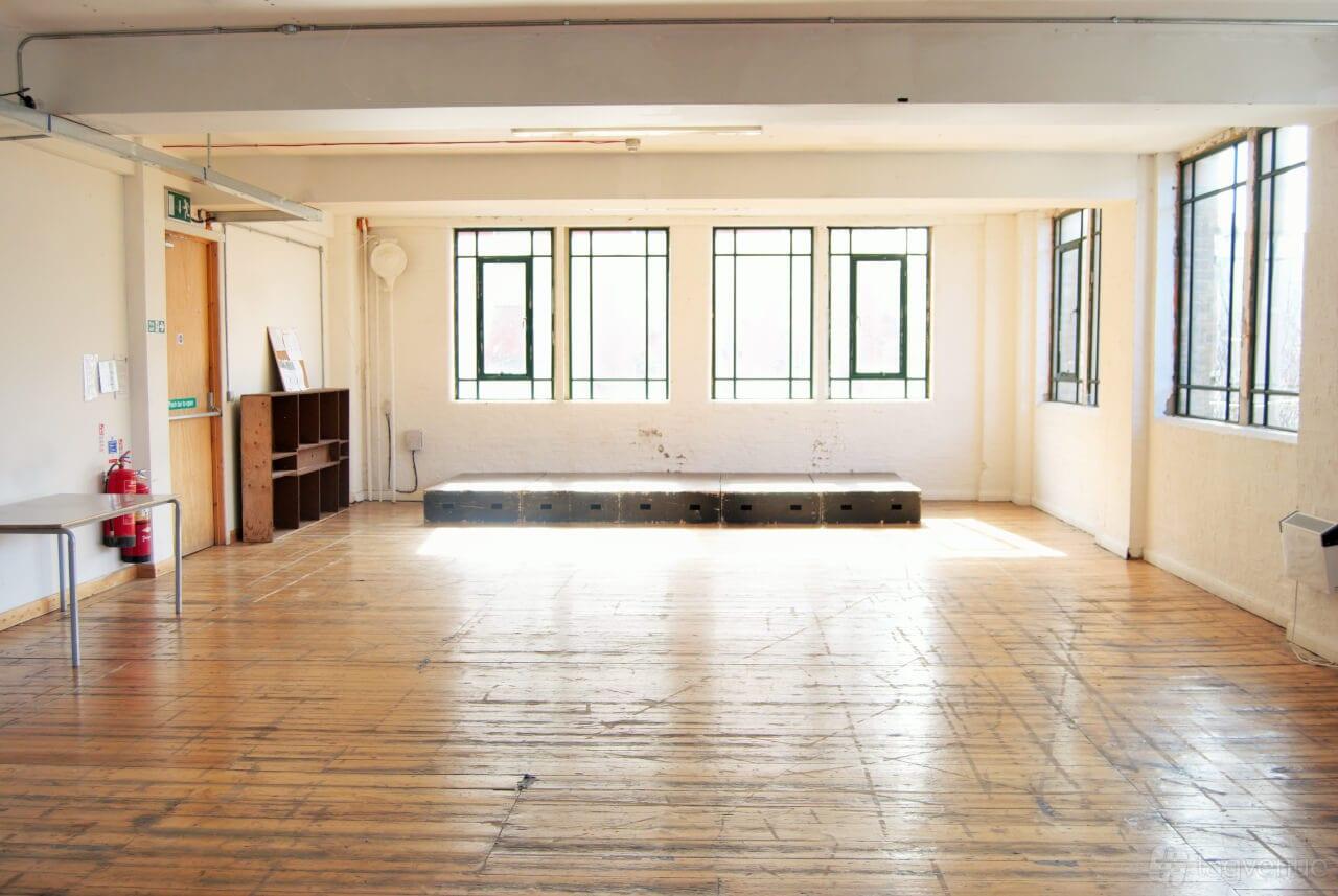 An event space with large windows, a small raised stage, and wooden floors at Arcola Theatre & Bar.