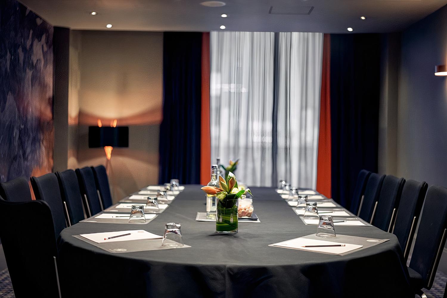 A hotel dining room with a long boardroom table, black chairs, notepads, water bottles, and floral centerpieces at Malmaison Liverpool.
