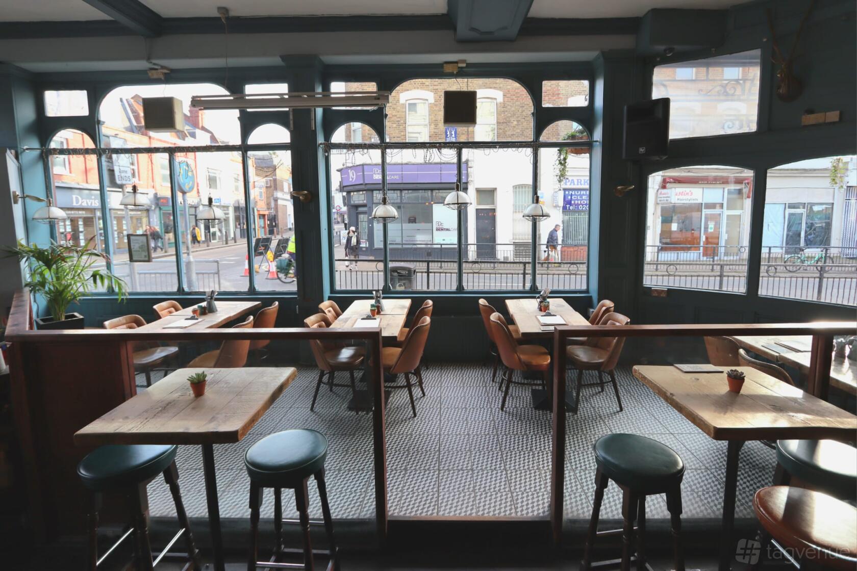 A bar with large arched windows, tiled floors, and wooden tables with chairs at The Regent Balham.