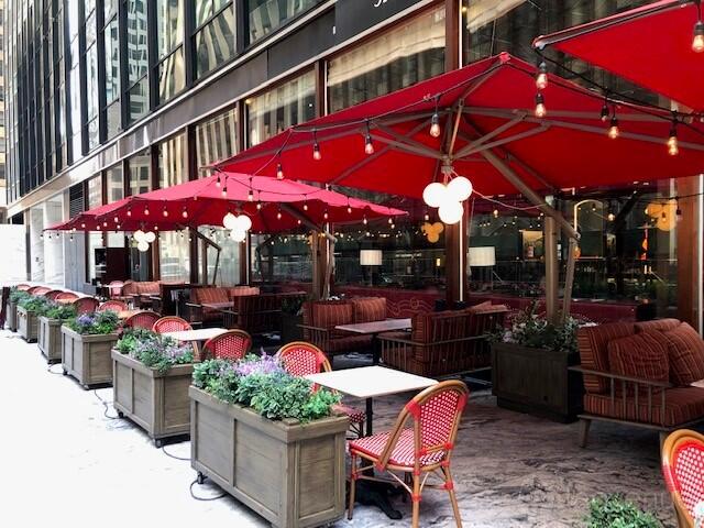 An outdoor restaurant patio with red umbrellas, string lights, and red bistro chairs at Redeye Grill.