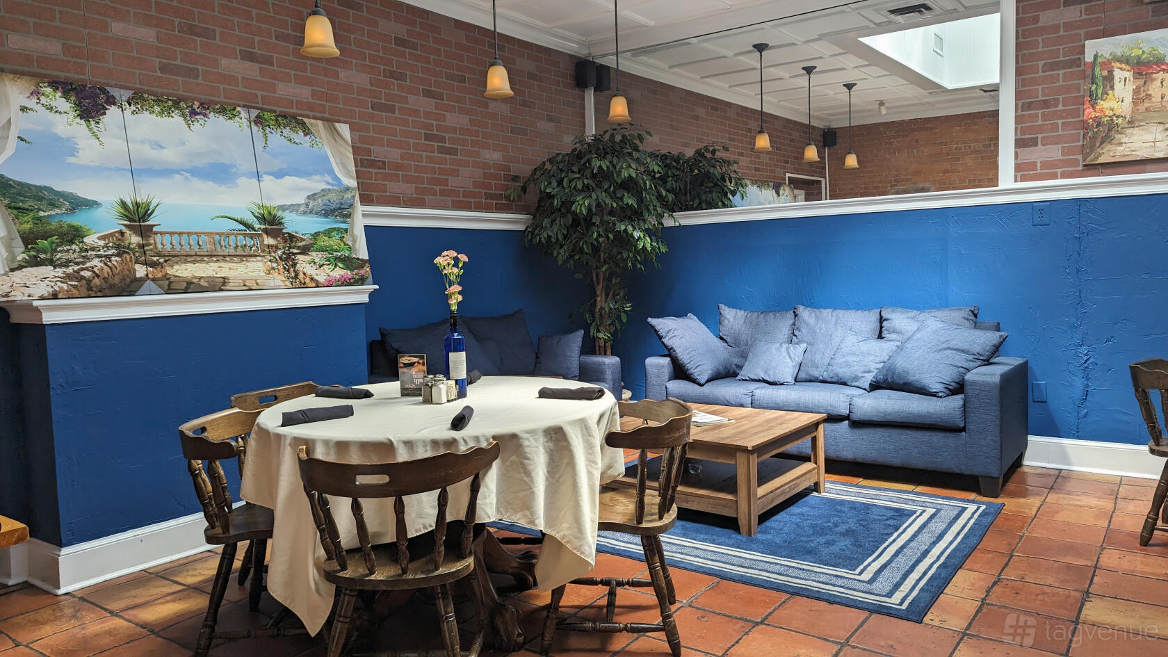 An event space in a restaurant with exposed brick walls, blue accent wall, round table, and cushioned sofa at Mylo's Grill.