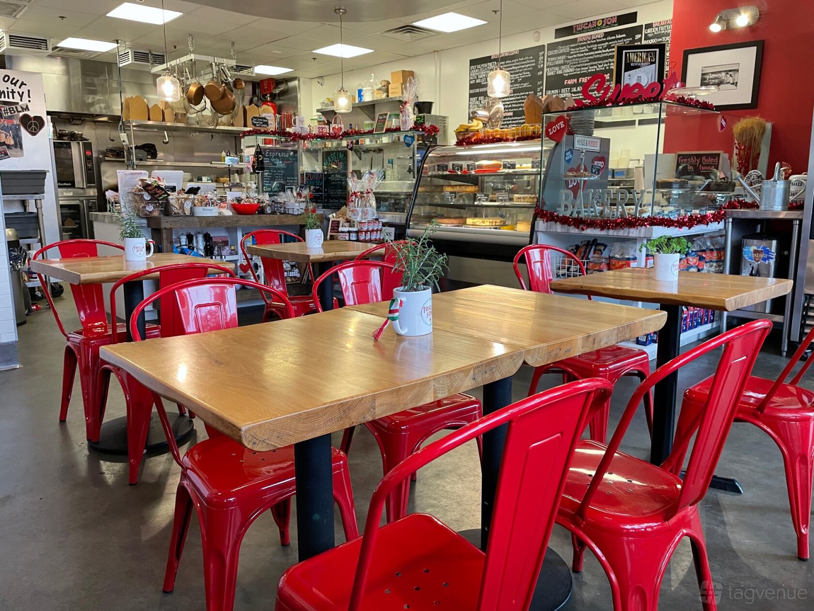 A restaurant with wooden tables, red metal chairs, and an open kitchen counter at Tuscan Son.