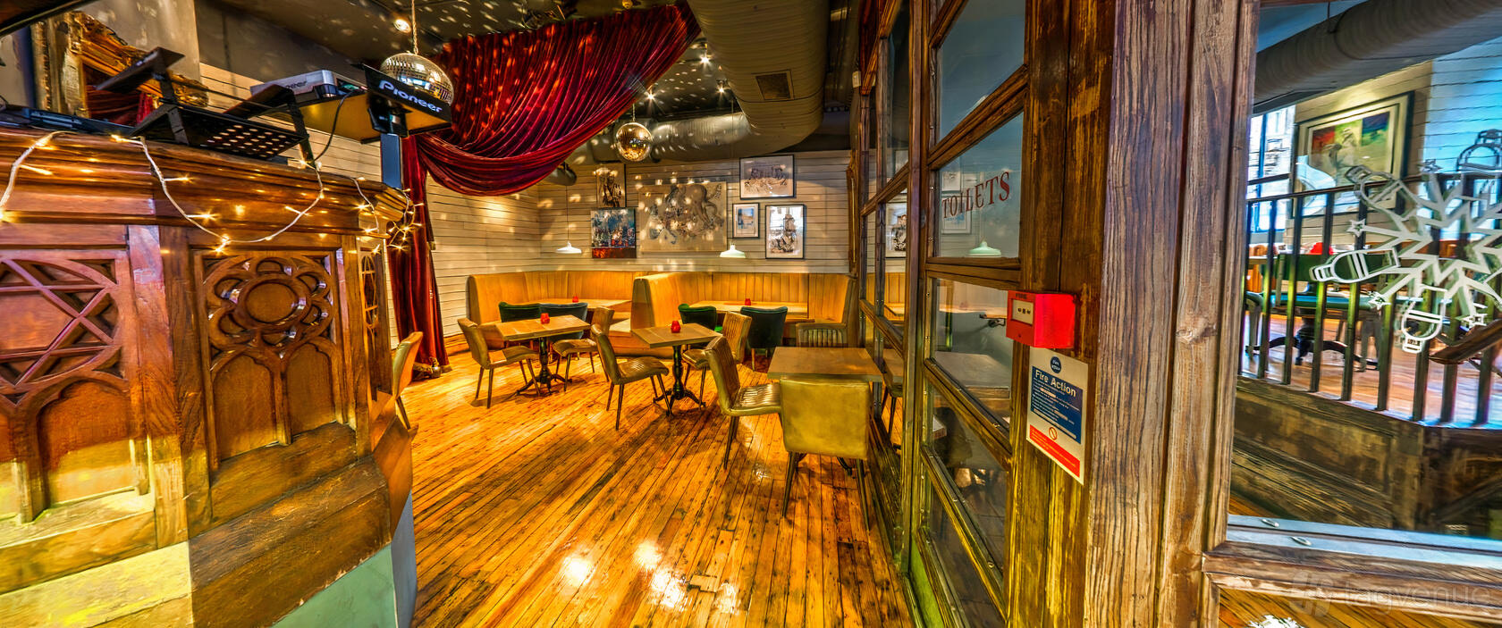 A bar with wooden floors, vintage armchairs around small tables, and hanging pendant lights at Revolution Glasgow - Renfield Street.