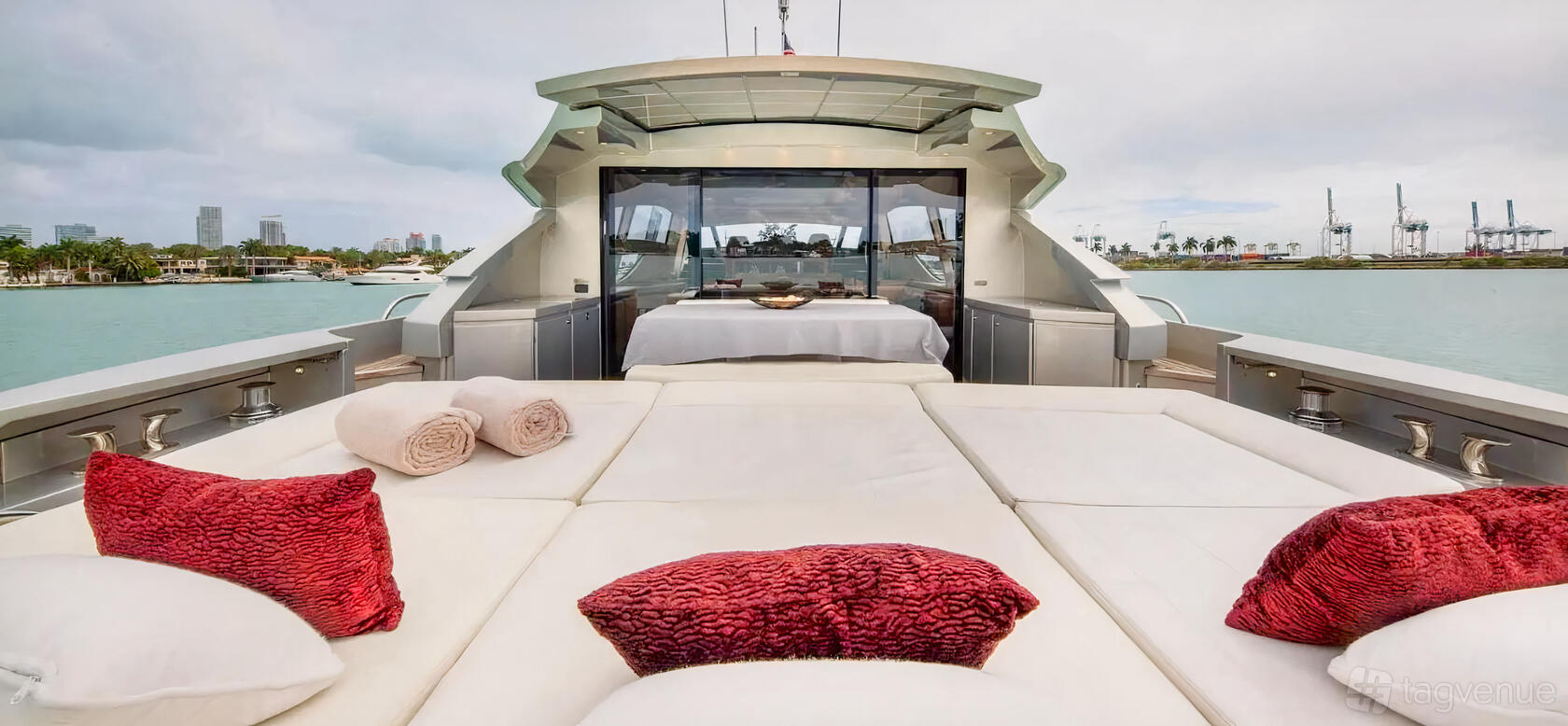 A luxury boat deck with white cushioned loungers, red accent pillows, and a table set at Beeyond Boats - Harbor West Marina Miami.