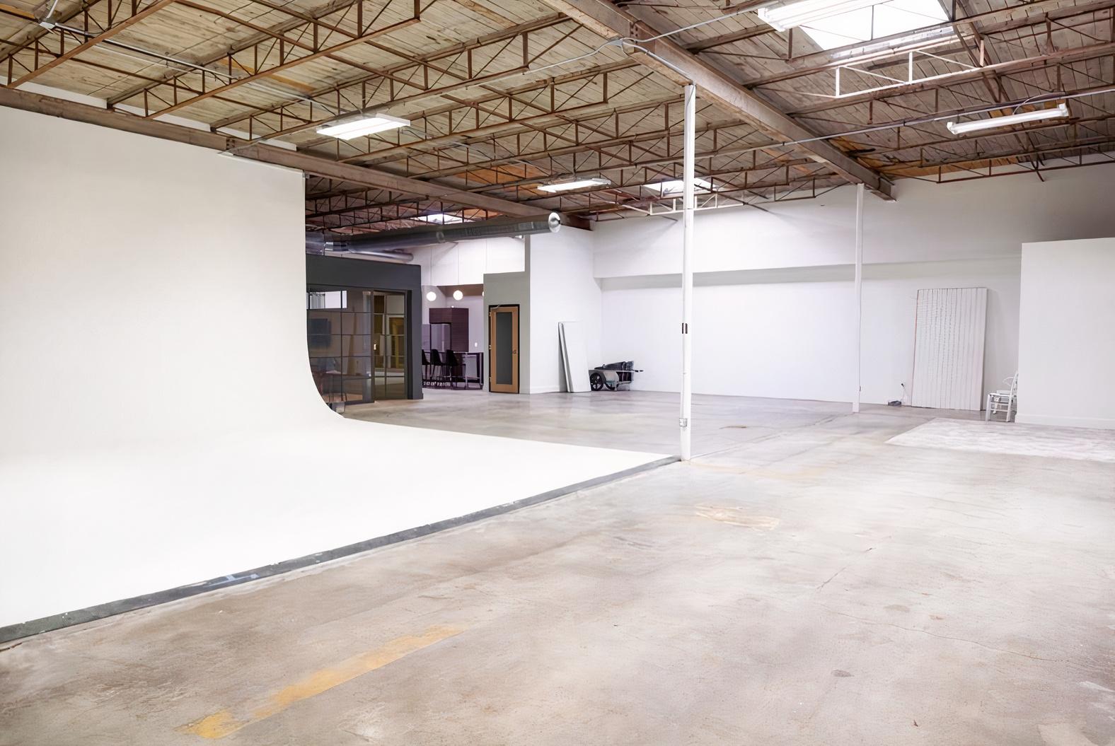 A photo studio with a large white cyclorama wall, high ceilings, and exposed beams at Terminus Studios.