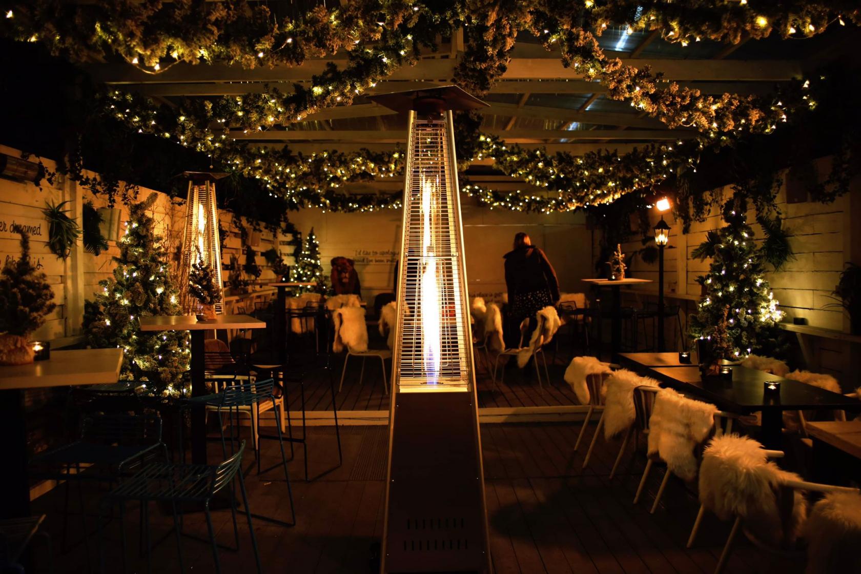 A terrace with fairy lights, floral garlands, patio heaters, and fur-covered seating at Exhibit.