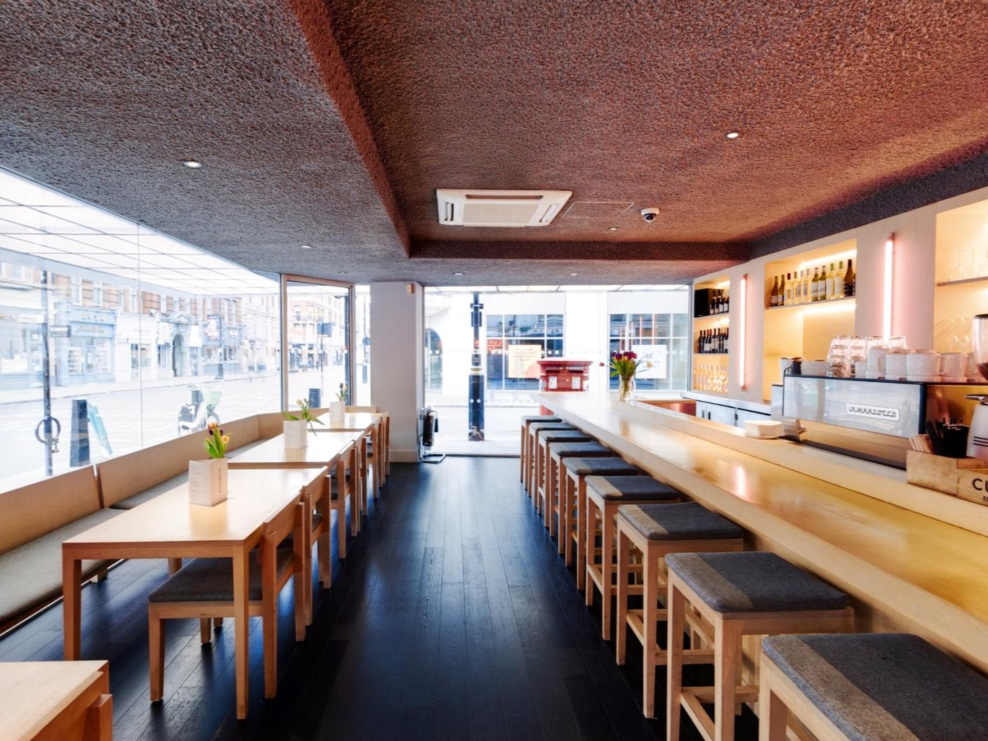 A cinema bar with long wooden tables, high stools, and floor-to-ceiling windows at Curzon Soho.