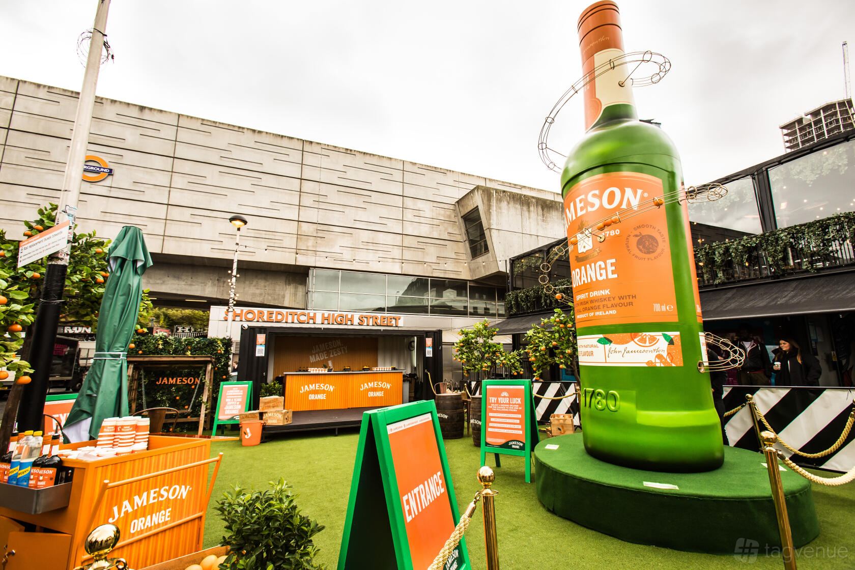An outdoor restaurant space with artificial grass, branded signage, seating, and a large Jameson bottle at Boxpark Shoreditch.