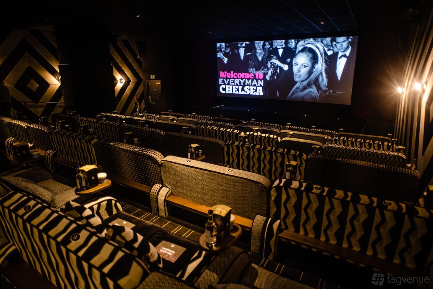 An auditorium with patterned armchairs, side tables, and a large projection screen at Everyman Chelsea.