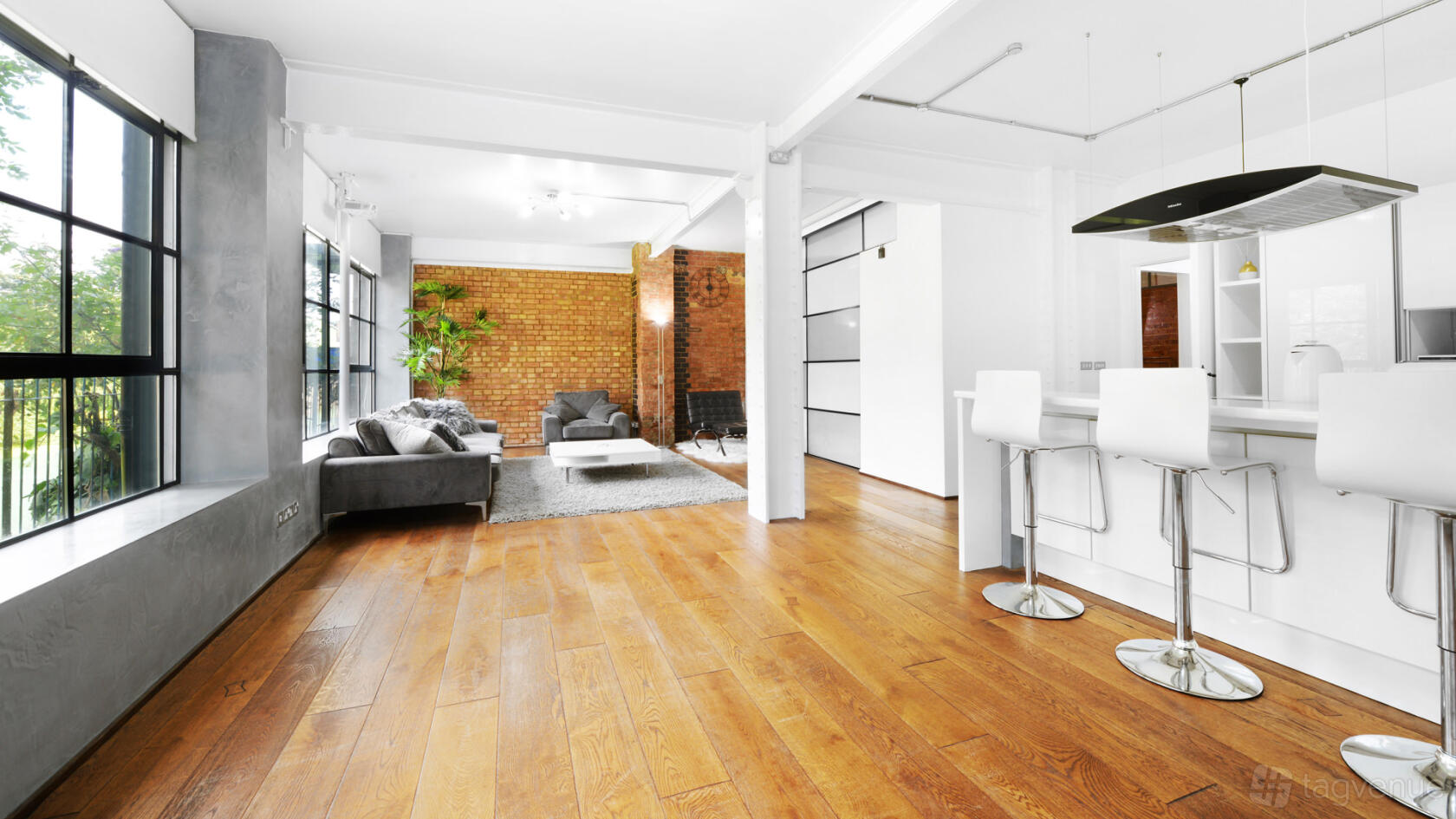 An apartment with large windows, exposed brick walls, hardwood floors, and a modern kitchen island at S1 Apartment.
