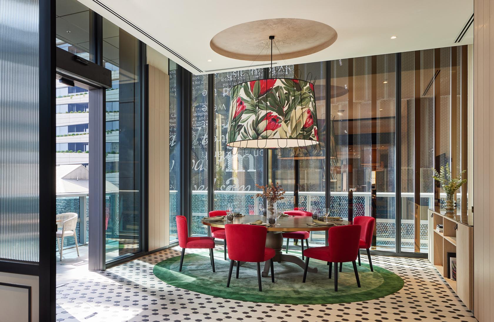 A hotel dining room with floor-to-ceiling windows, a floral pendant light, and a round table with red chairs at Dorsett Melbourne.