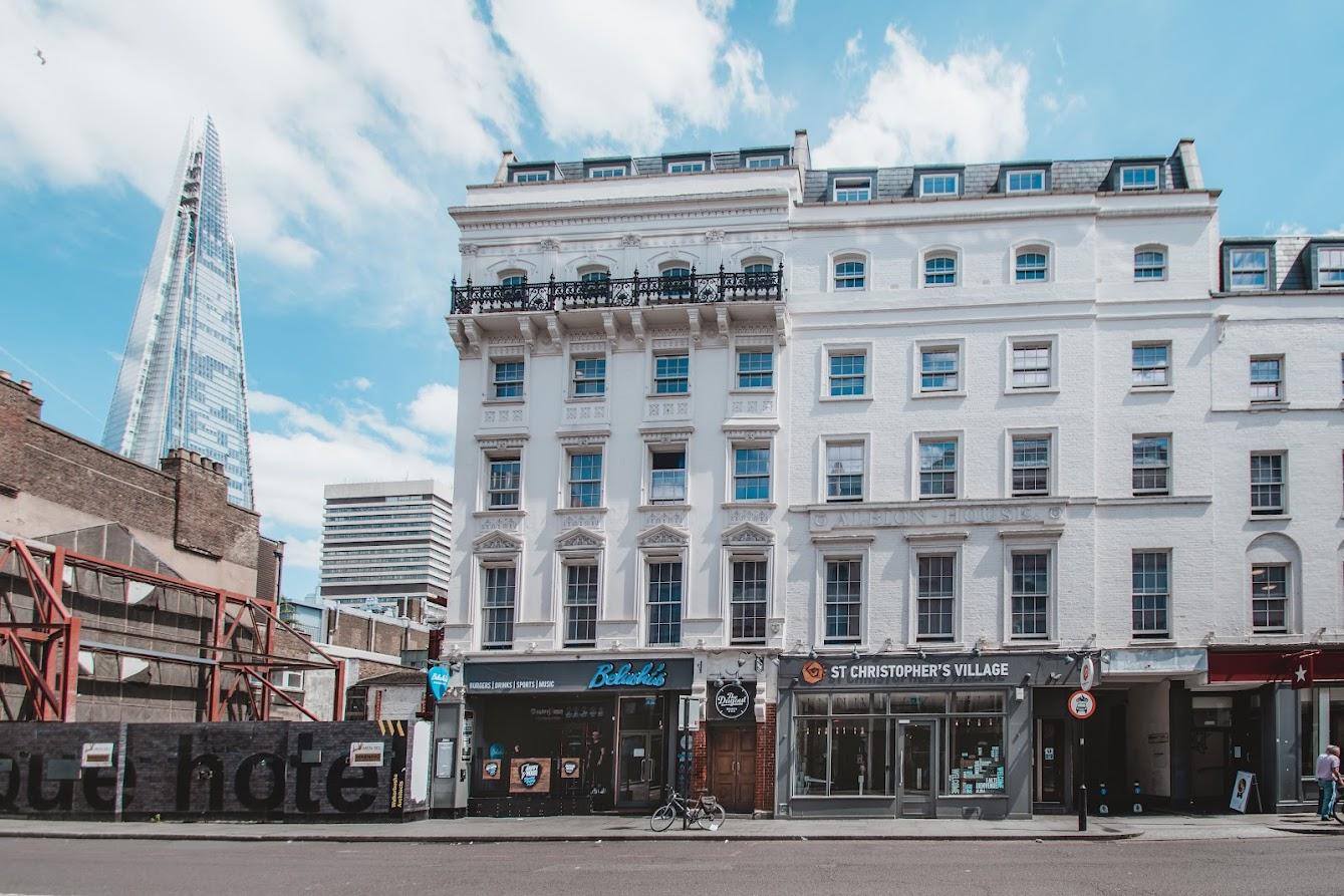 A white-painted pub and bar with ornate windows and The Shard visible in the background at Belushi's & The Dugout London Bridge.