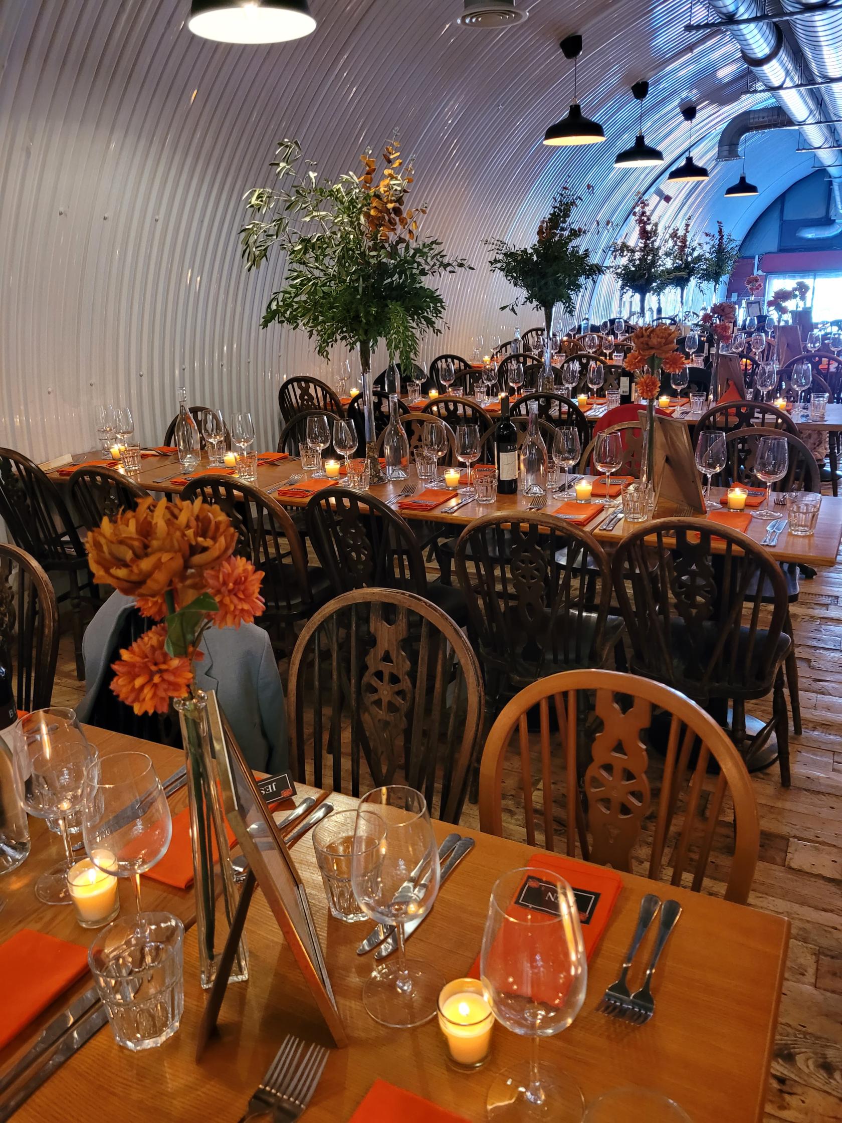A bar with long wooden tables, mismatched chairs, candles, and glassware set for dining at Pedro's Wine Bar.