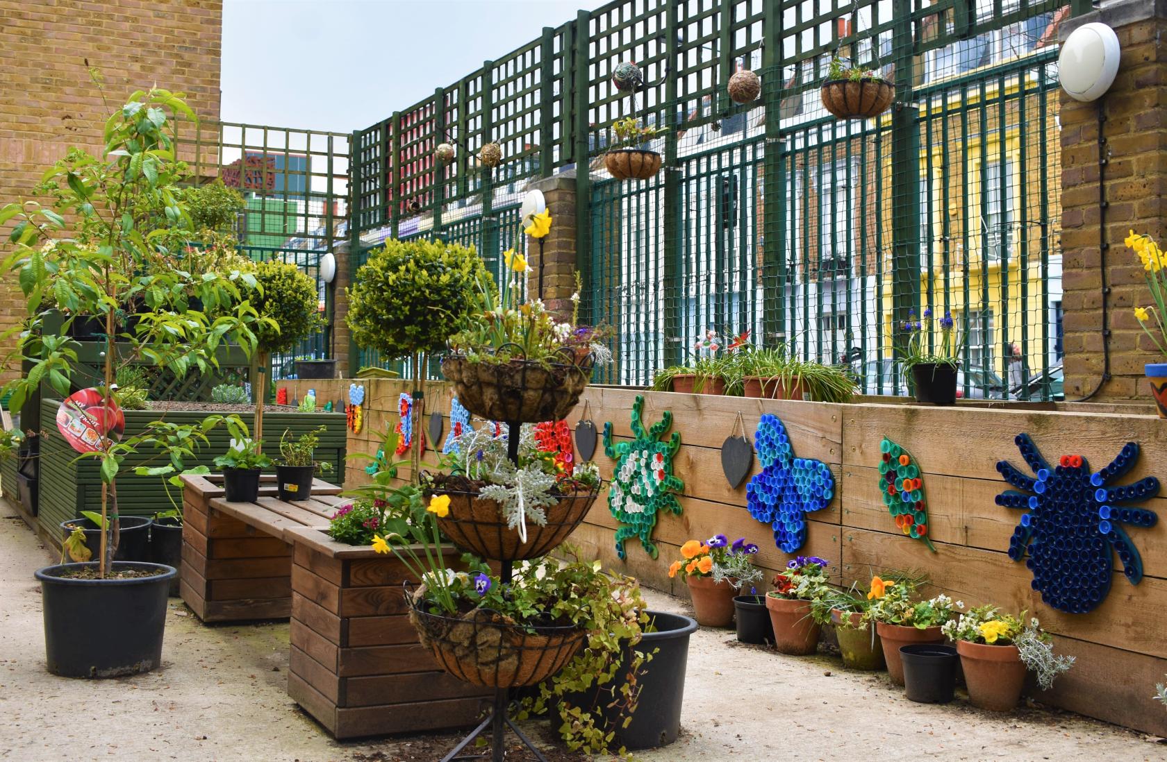 An outdoor community centre space with raised wooden planters, potted plants, and colorful recycled art at Castlehaven Community Centre & Hub.