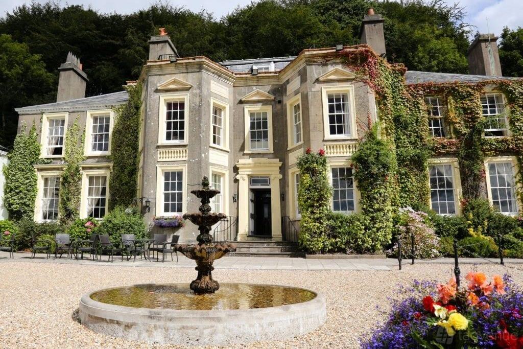 A historic hotel with ivy-covered stone facade, central tiered fountain, and outdoor seating at New House Country Hotel.