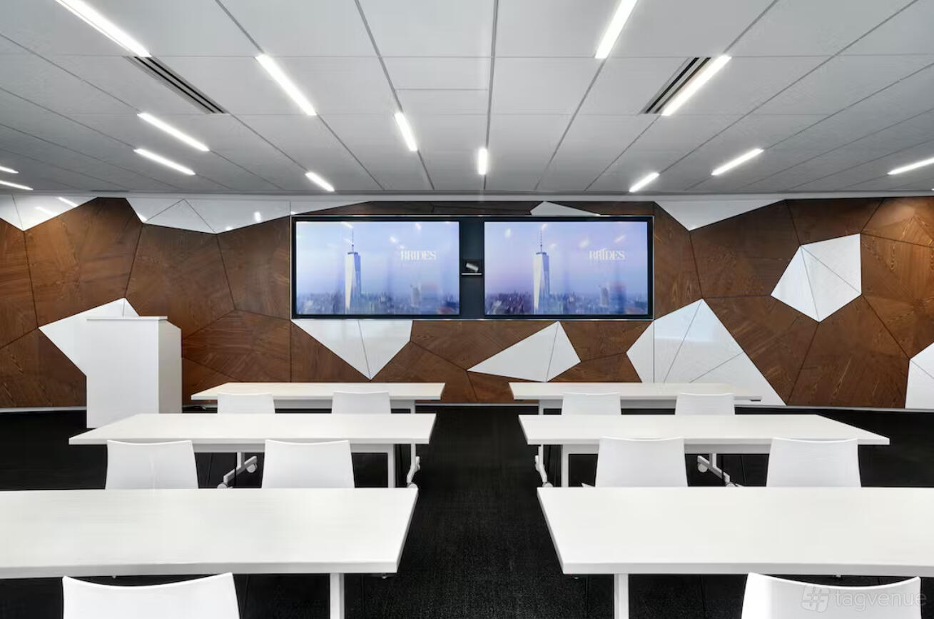 A coworking space with geometric wood wall panels, dual large screens, and white desks at Well& by Durst.