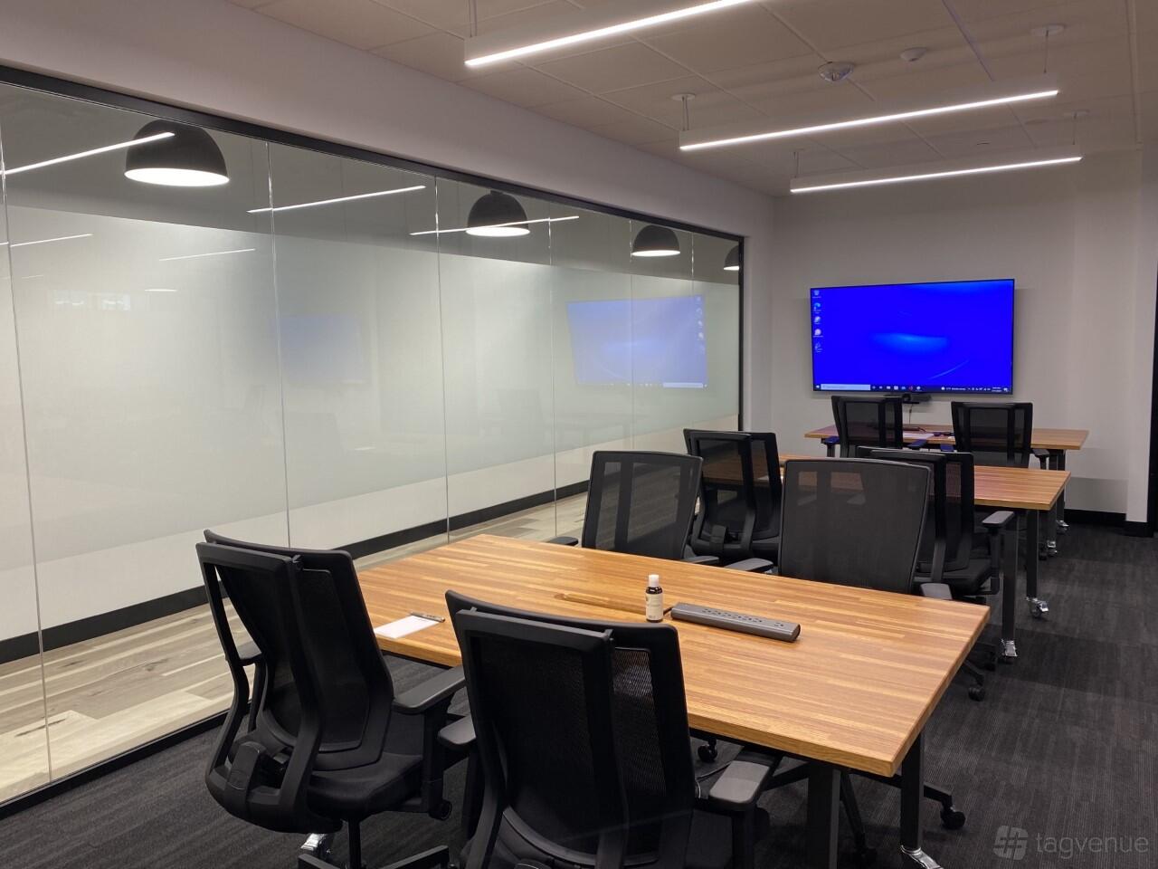 A training room with wooden tables, black mesh chairs, and a wall-mounted screen at Venture X Arlington - Courthouse Metro.