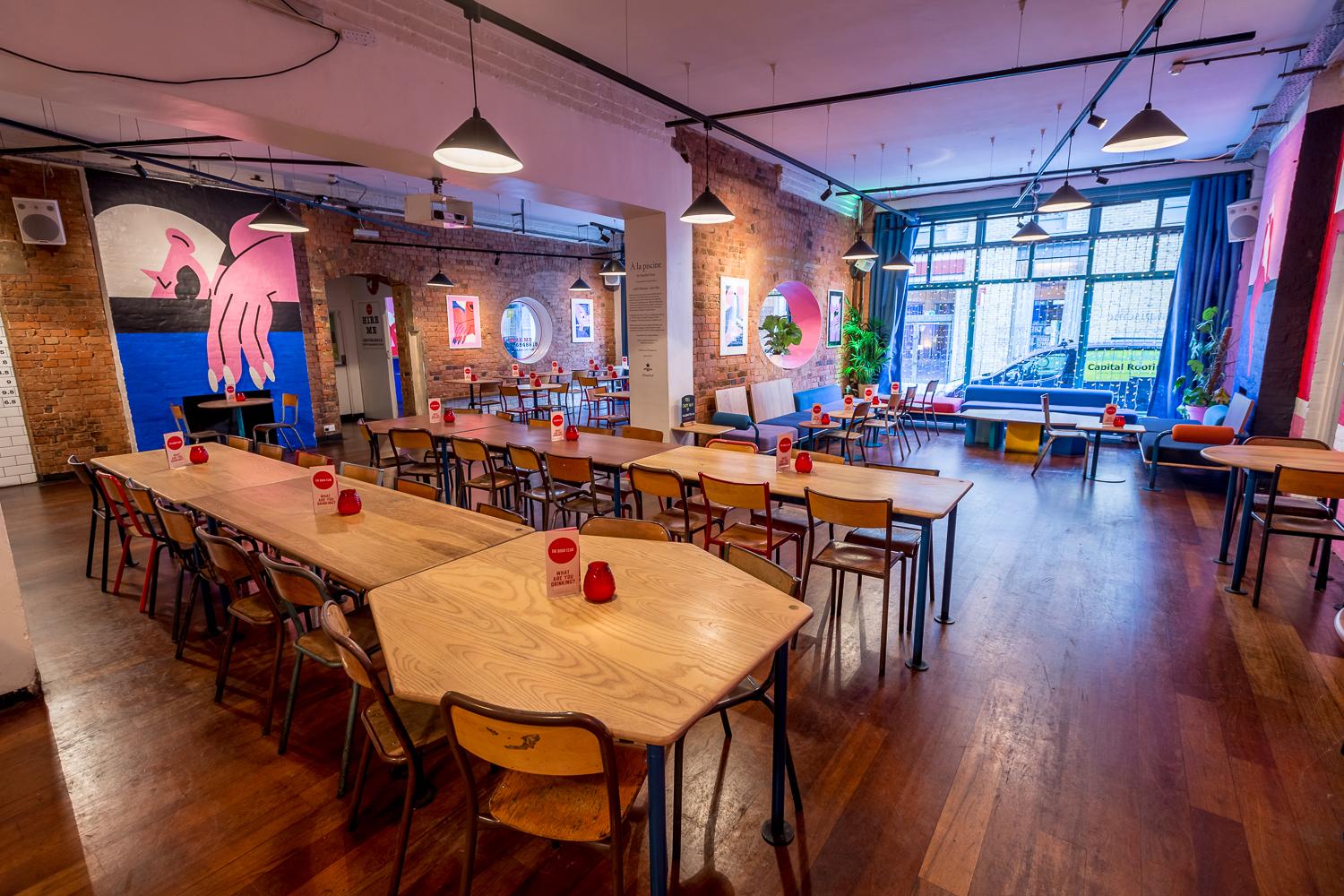An event space in a bar with exposed brick walls, colorful murals, and long wooden tables at The Book Club.
