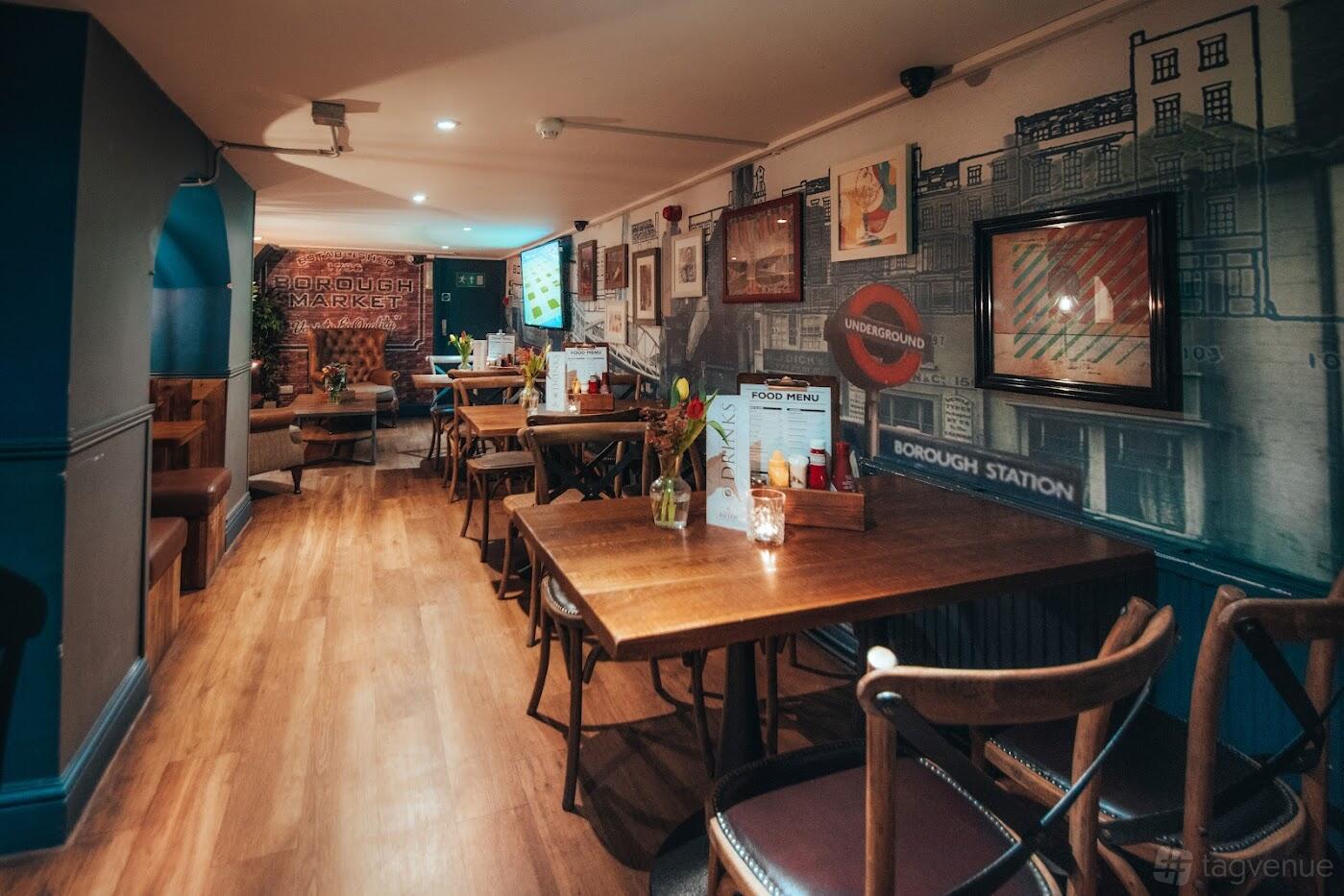 A function room in a pub with wooden flooring, mural-covered walls, and wooden tables at St Christophers Inn.