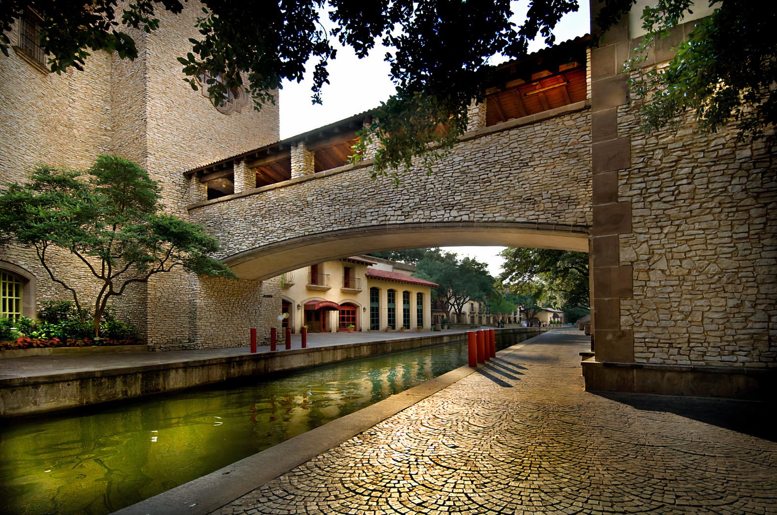 A hall with arched stone architecture and a shaded terrace overlooking a tree-lined canal at The Venetian Terrace.