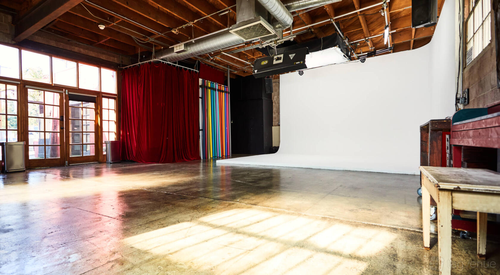 A photo studio with a pre-lit white cyclorama wall, concrete floors, exposed wood ceiling, and red curtains at Cherry Soda Studios.