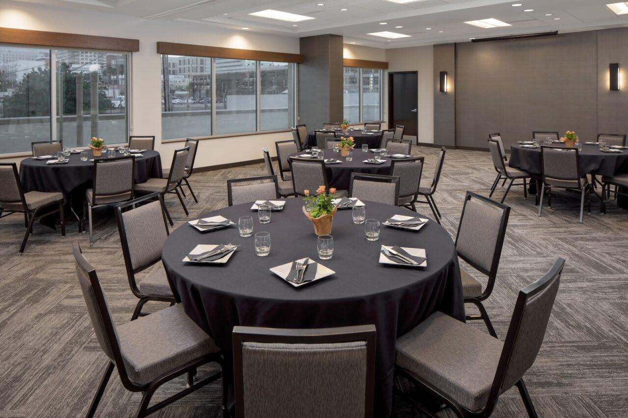 An event space with round tables covered in black linens, banquet chairs, and large windows at Hyatt Place Glendale/Los Angeles.