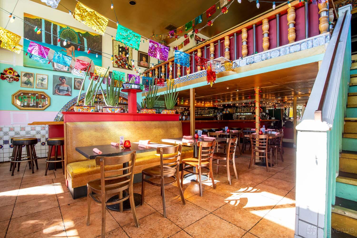 A restaurant with colorful papel picado banners, wooden chairs, and mezzanine seating at El Condor.