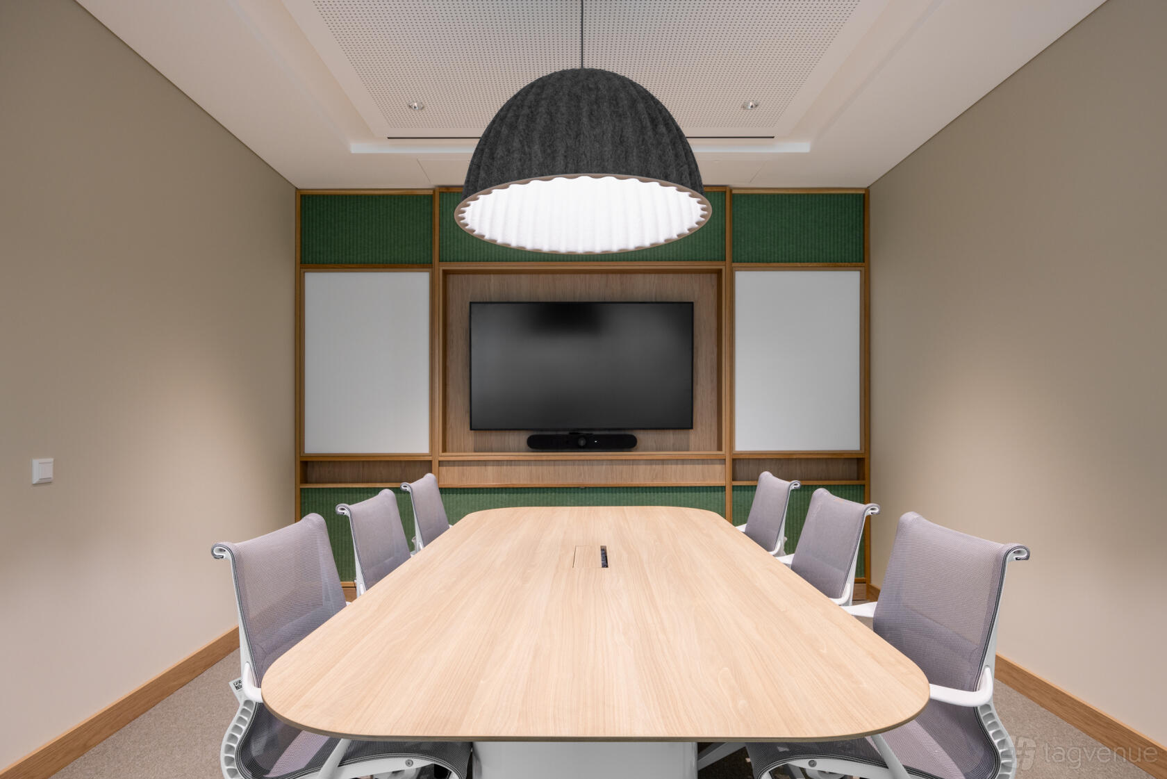 A meeting room with a wooden conference table, gray chairs, large pendant light, and wall-mounted TV at The Work Project at Goulburn Street.
